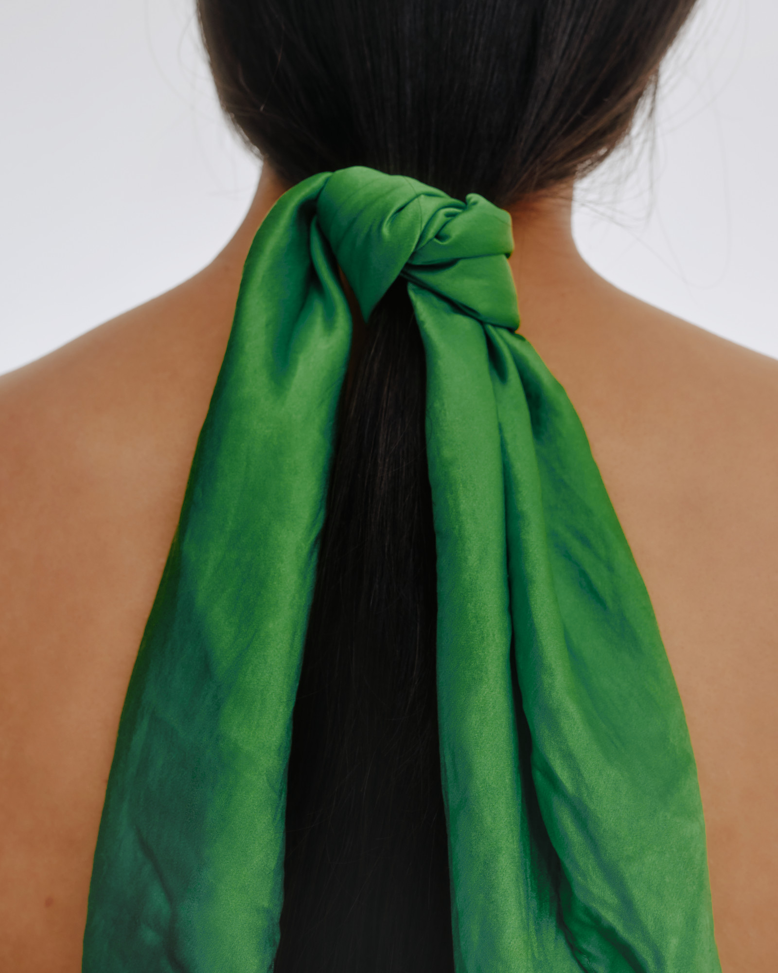 Back of a person's neck with long dark hair tied with a green scarf or fabric.