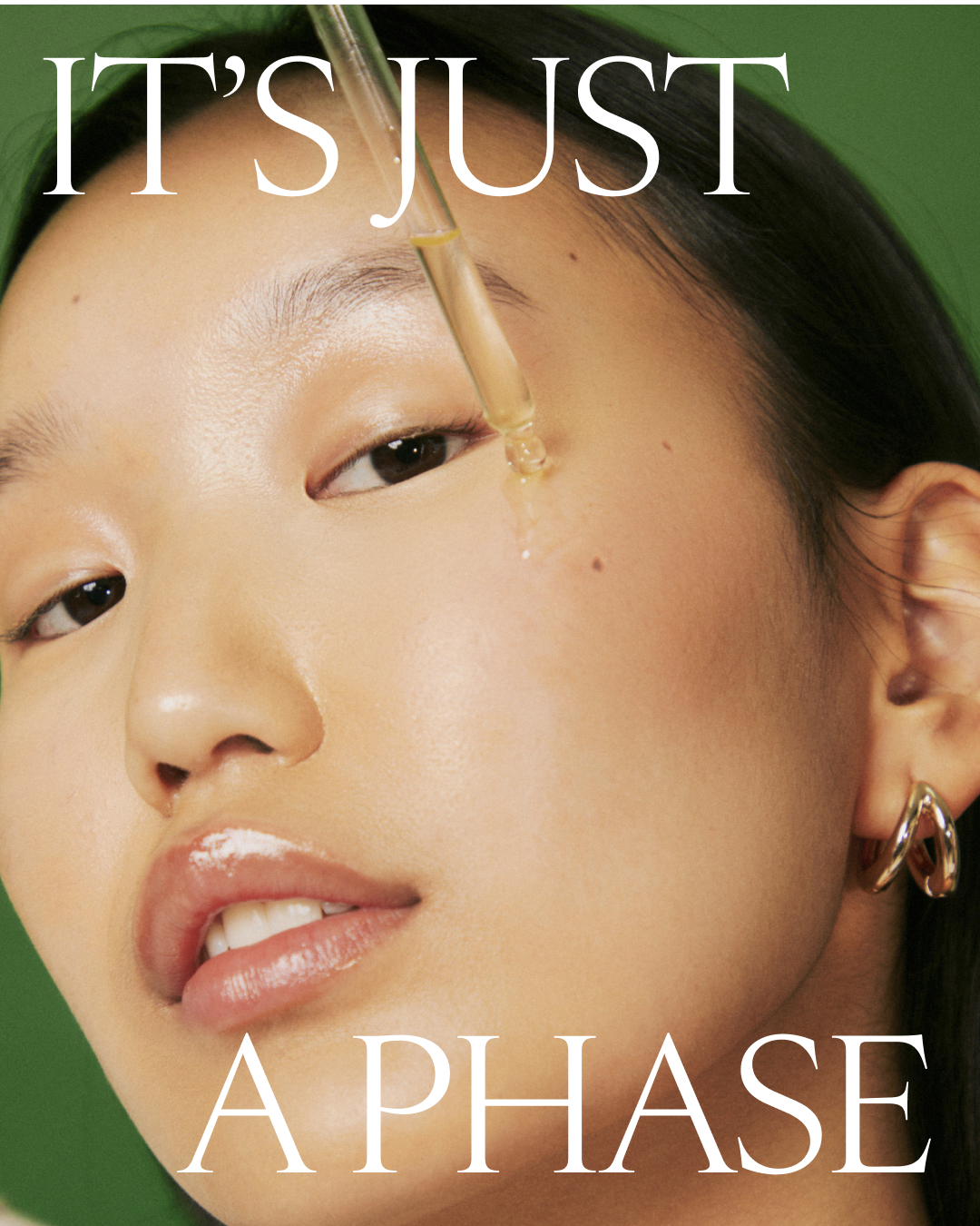 A close-up of a woman's face with skincare serum being applied near her eye. She has clear skin, minimal makeup, and is wearing gold hoop earrings. The background is green. The text overlay says "IT'S JUST A PHASE."