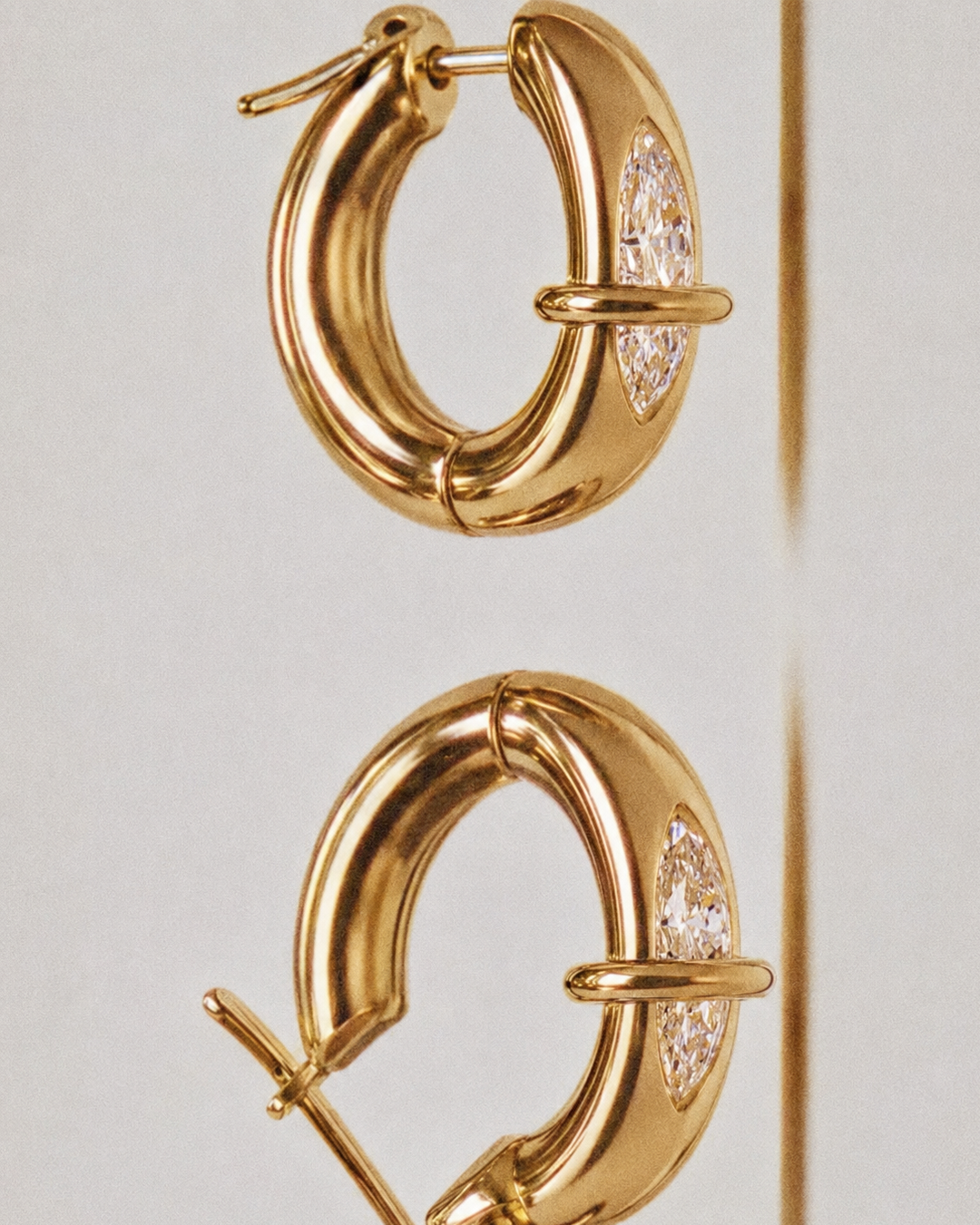 Gold hoop earrings with diamonds, hanging with a plain background