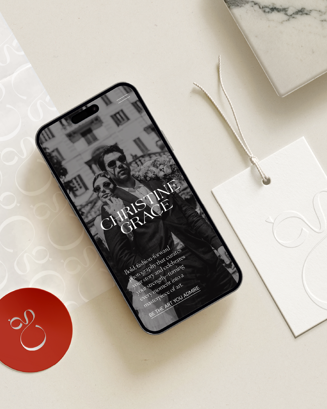 Smartphone displaying a mobile website design for Christine Grace, on a white desk with branded elements and a white tag.