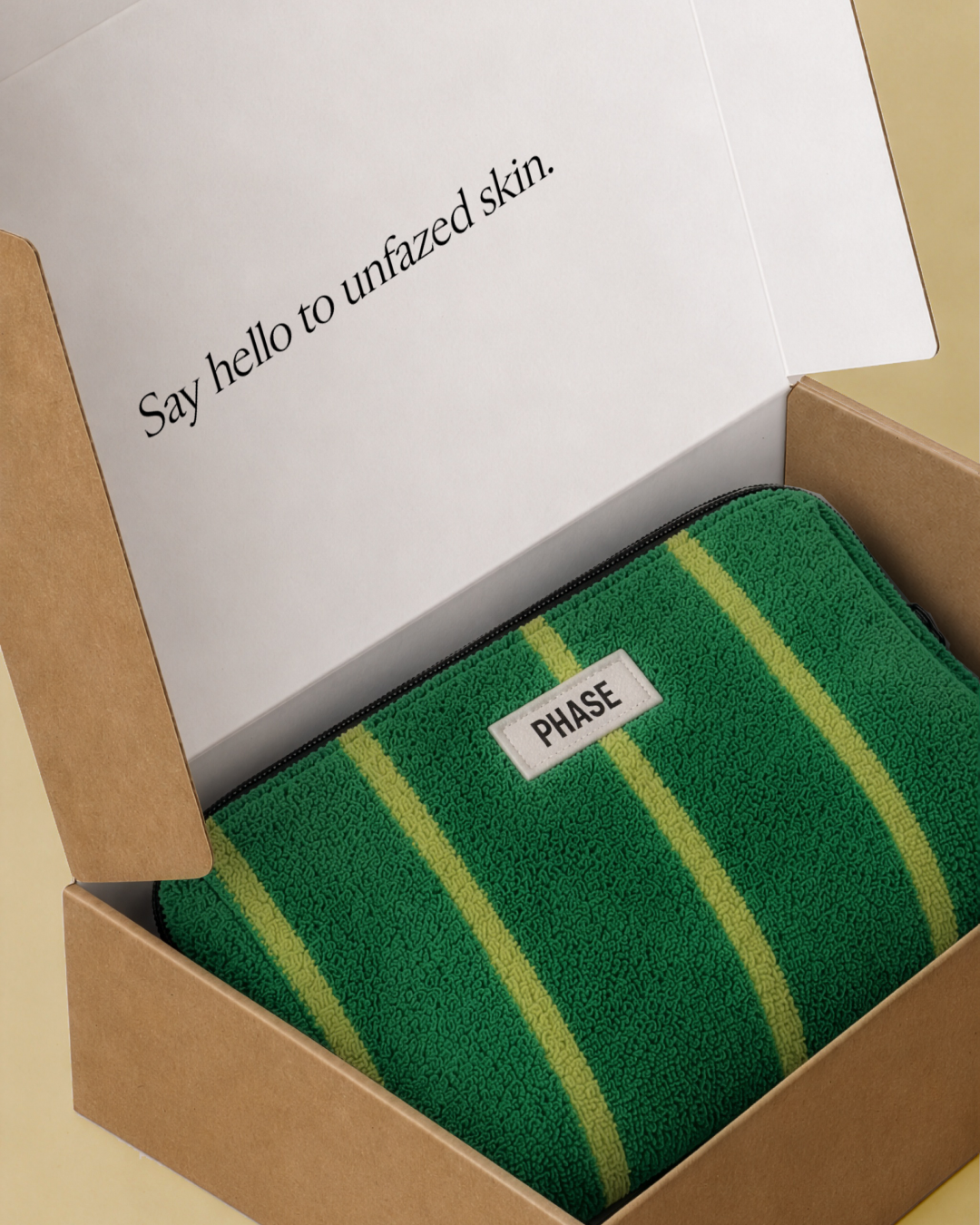 A branded box with an inside message that says "Say hello to unfazed skin." The box contains a green and yellow striped cloth pouch with a branded label for Phase skincare.