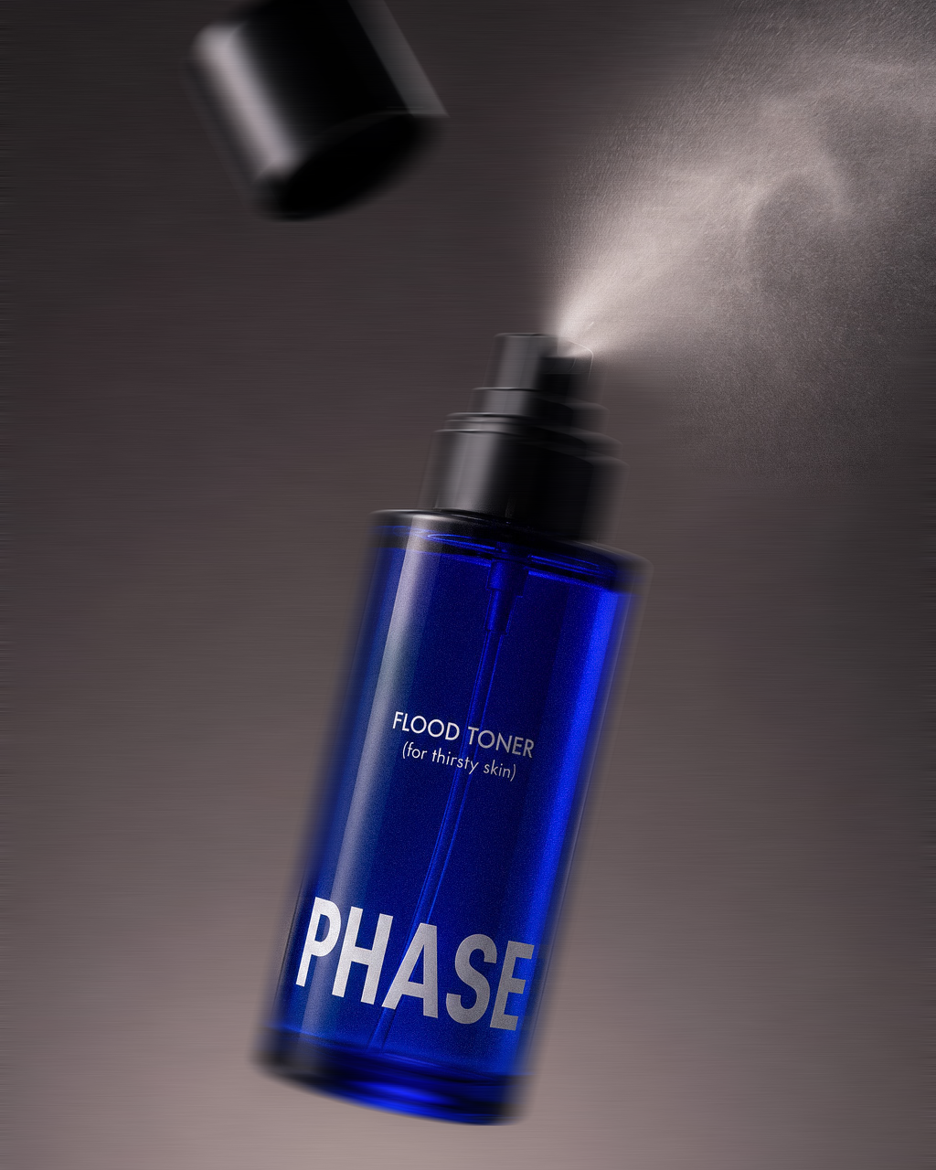 A blue bottle of Phase Flood Toner with a spray nozzle, spraying a fine mist.