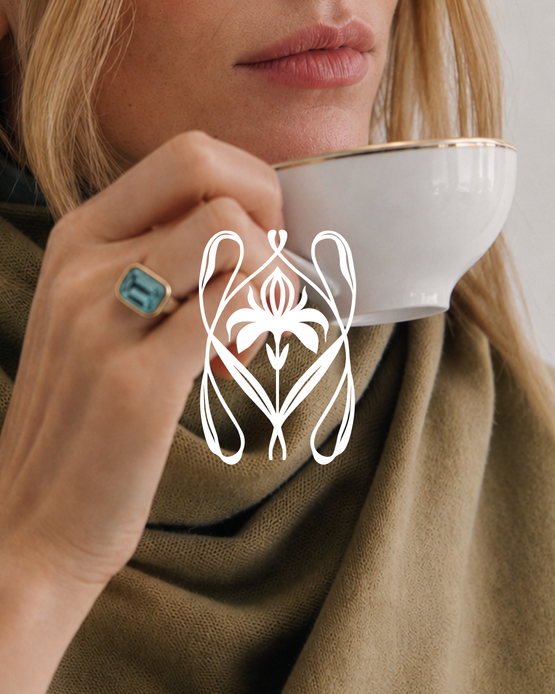 A woman with blonde hair drinking from a white teacup, wearing a beige scarf and ring with a turquoise stone, with an abstract H brand mark overlayed in white.