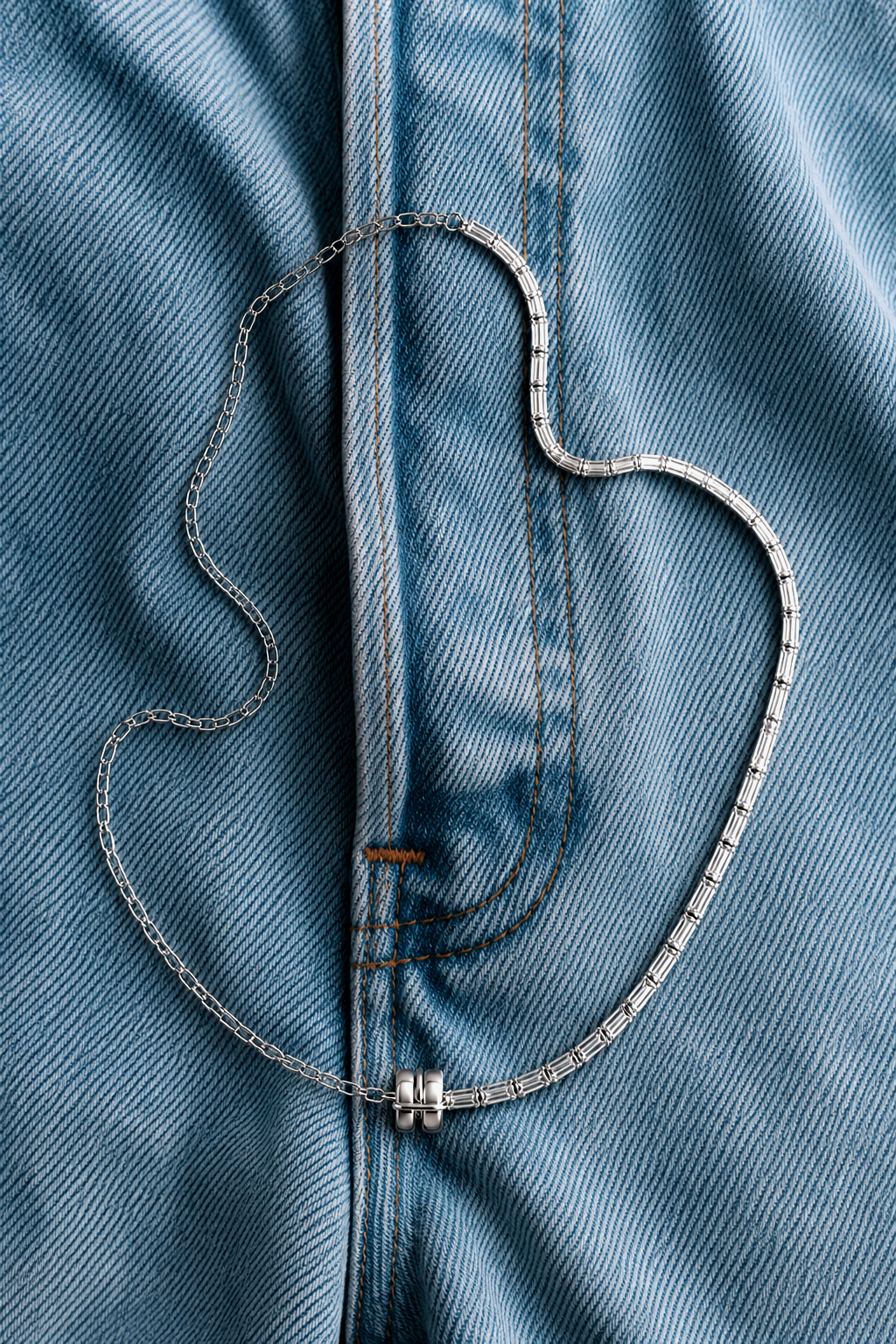 Silver necklace with rectangular diamonds lying on blue denim jeans.