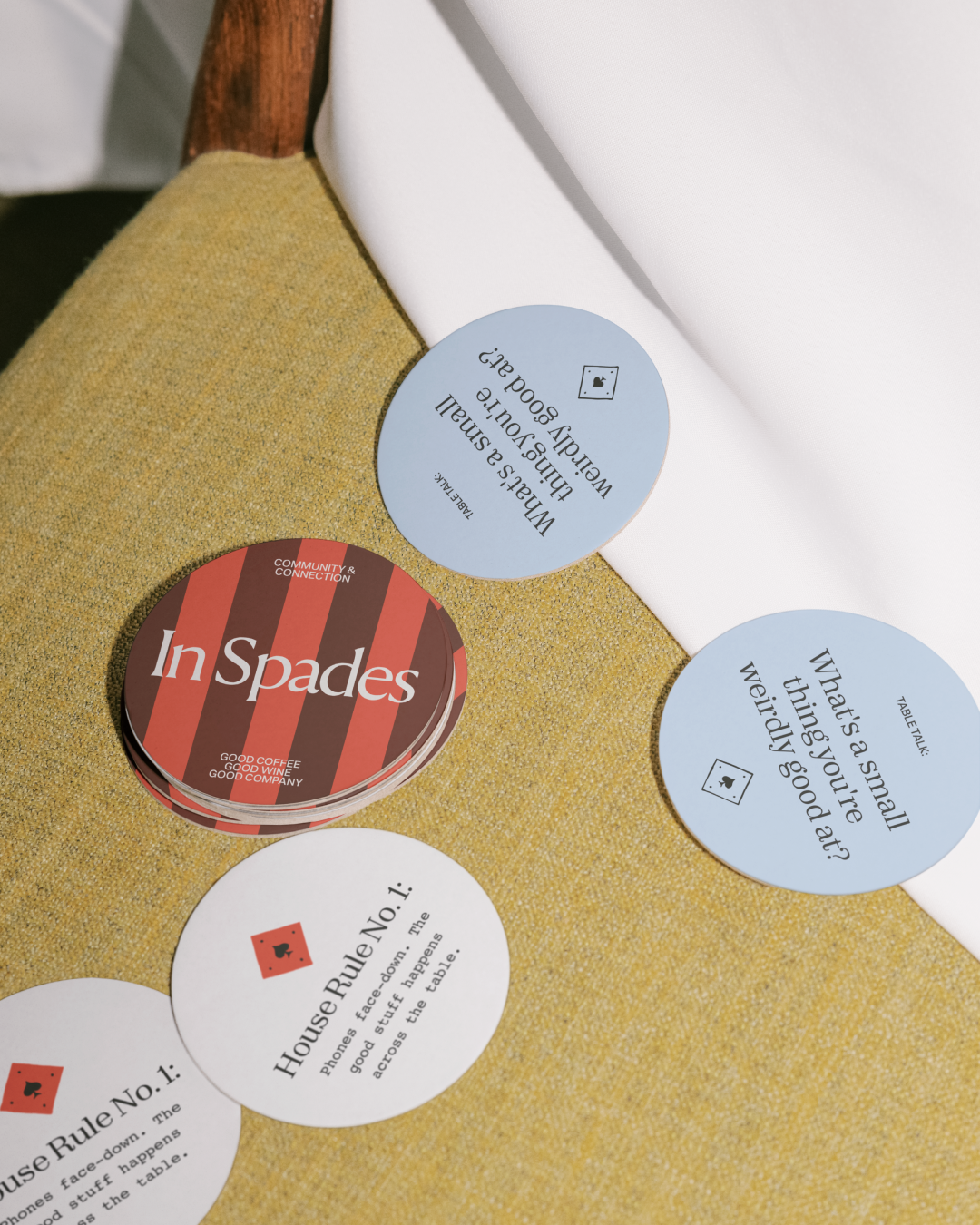 Stacks of branded coasters with questions and statements on a chartreuse chair, with a white tablecloth.