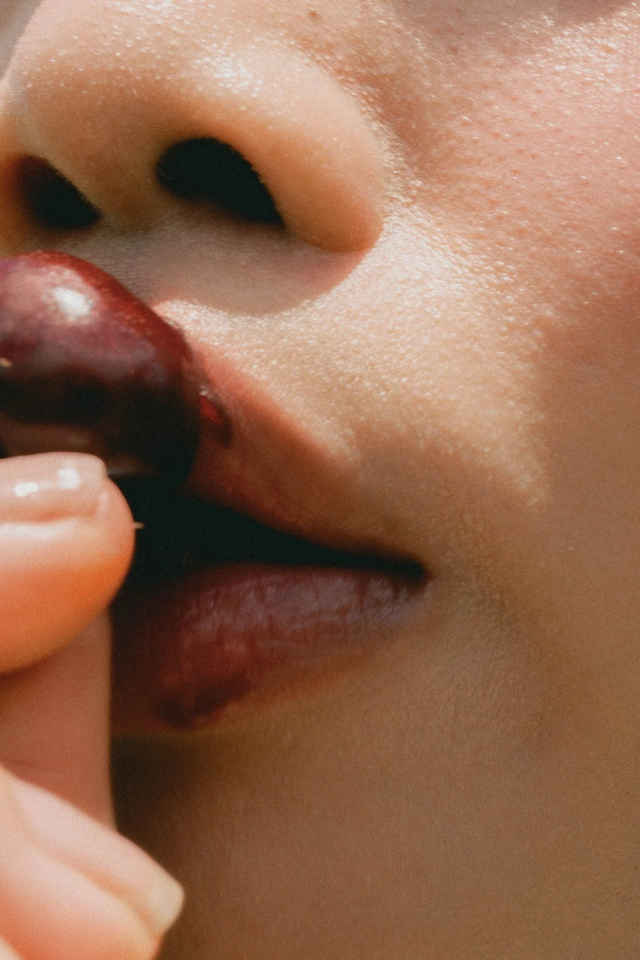 Close-up of a person's nose and lips, with a hand holding a cherry.
