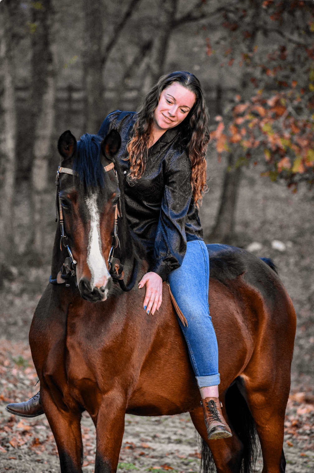 A woman riding a brown horse in a wooded area during autumn.