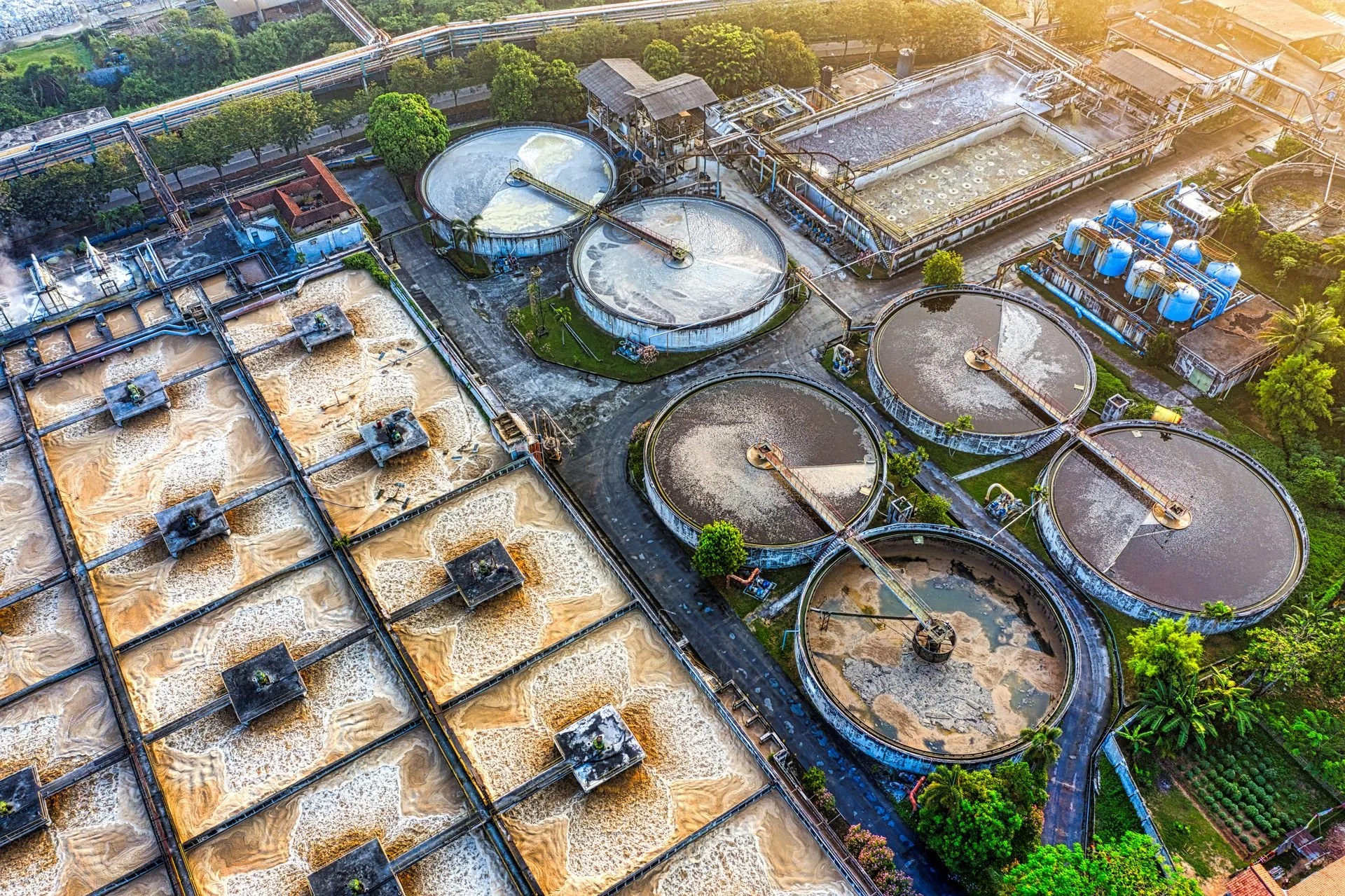 An aerial view of a wastewater treatment plant with large circular clarifiers, filtration basins, and processing equipment.