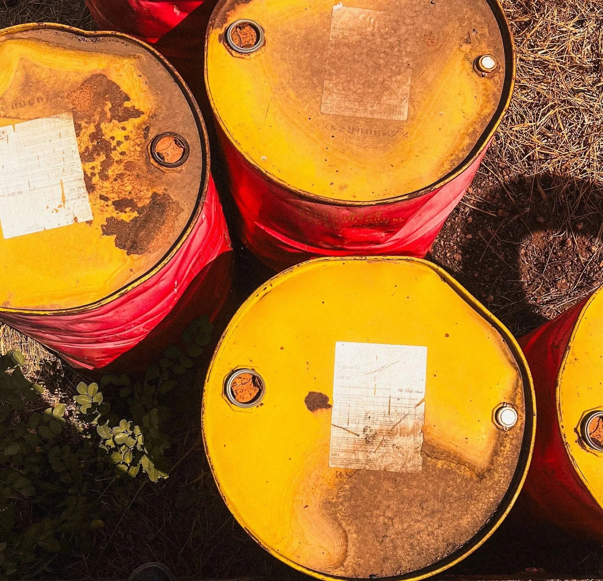 Three weathered industrial steel drums with yellow lids and red sides stored outdoors for hazardous material or chemical waste handling.