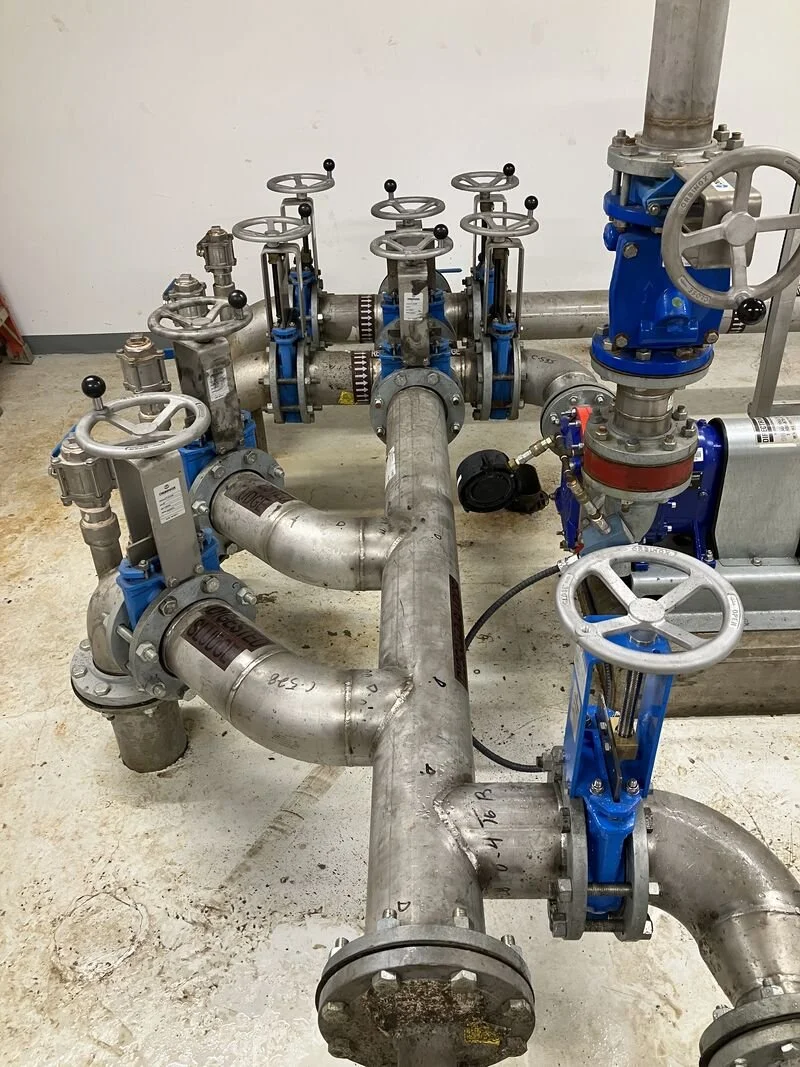 Industrial piping system with multiple valves, gauges, and fittings, installed on a concrete floor.
