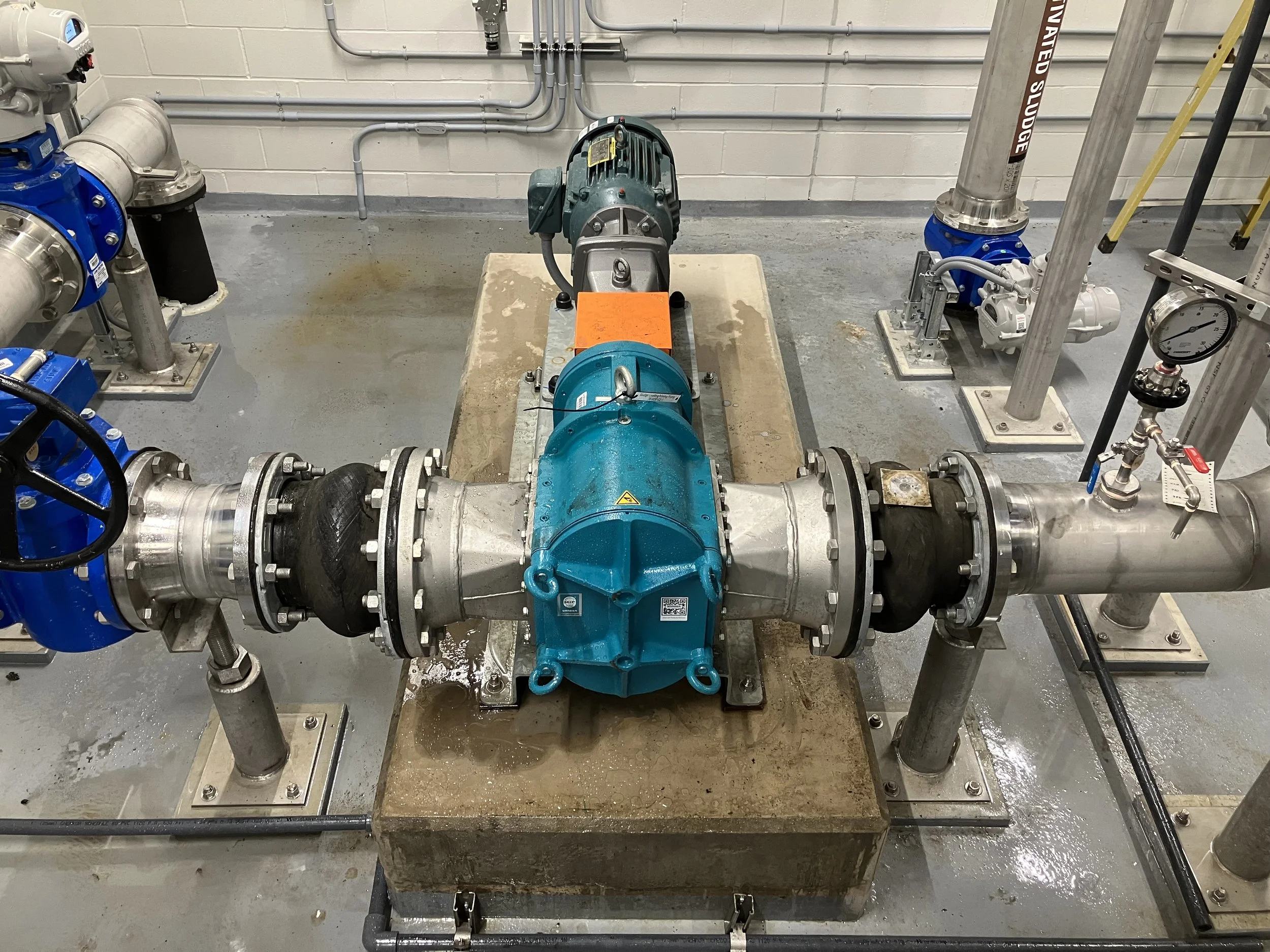 A large industrial pump system installed on a concrete platform, with pipes and gauges, in a mechanical or utility room.