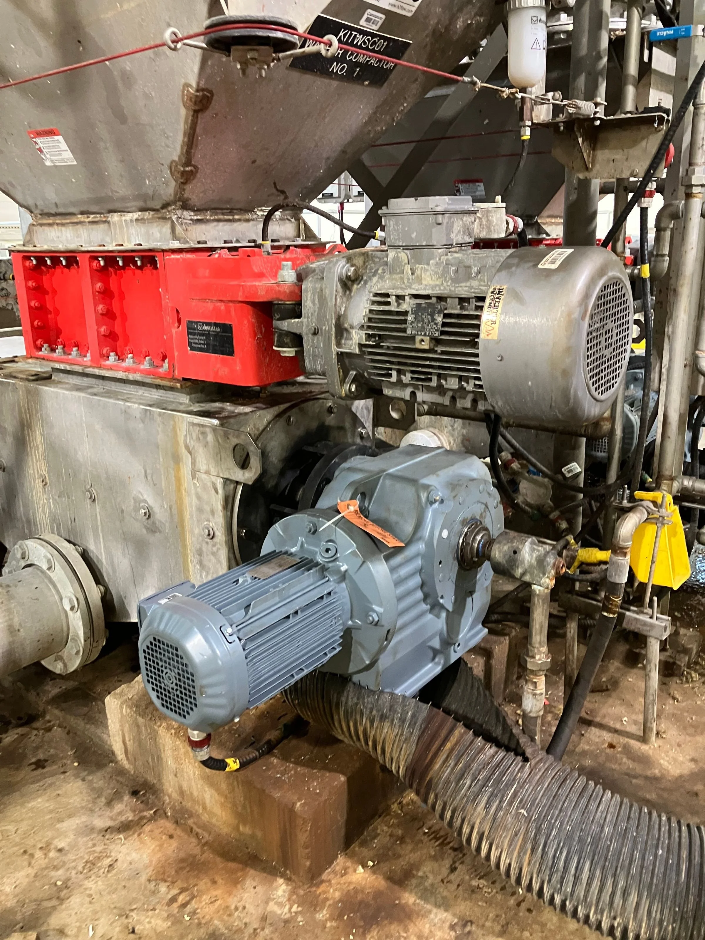 Industrial machinery including a motor, large red component, flexible ducting, and piping in a construction or maintenance setting.