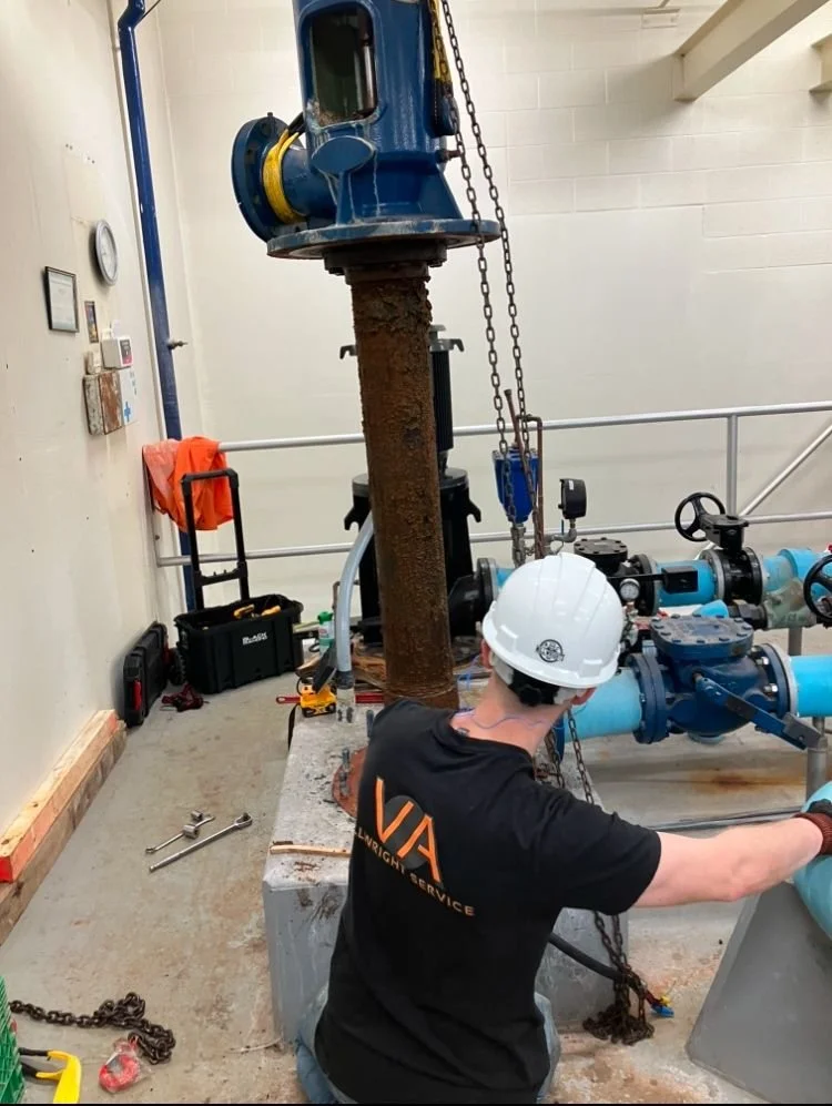 Worker in a hard hat working on industrial pipes and machinery in a facility.