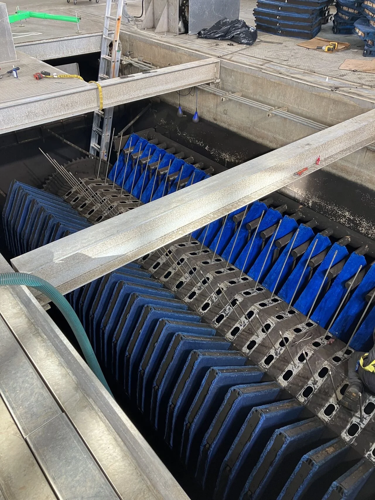 A metal industrial water treatment tank with blue filter plates, pipes, and a ladder at a construction site.