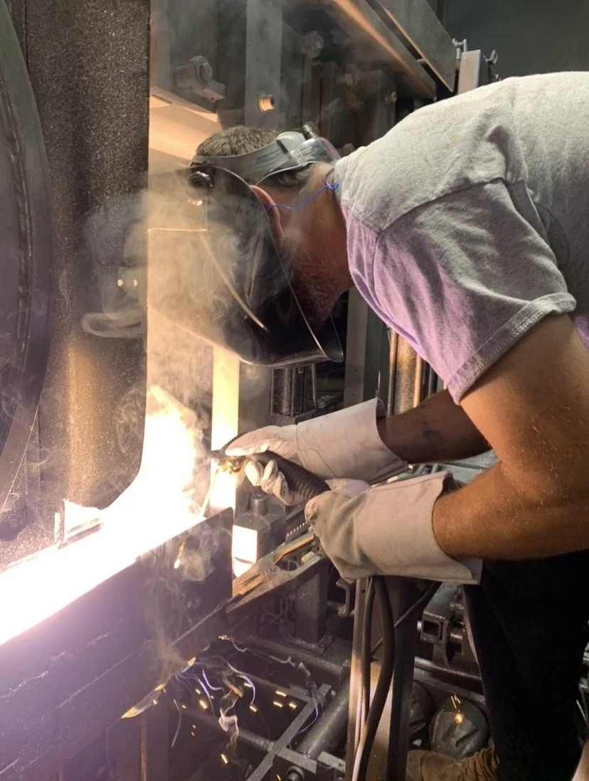 Man welding metal with protective helmet and gloves in a workshop.