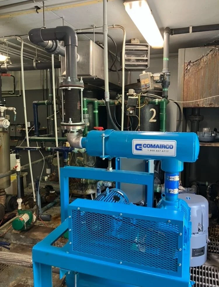 Industrial water treatment equipment with pipes, valves, and a blue Comairco filtration system in a mechanical room.
