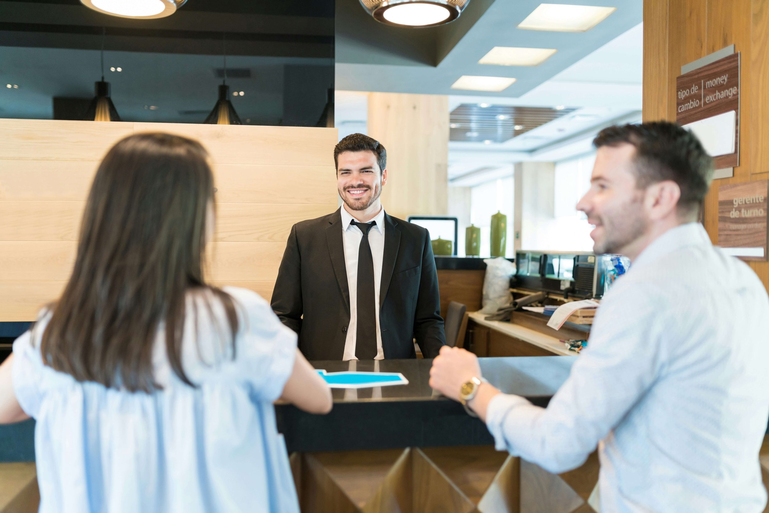 A hotel receptionist in a suit smiling at a group of guests in the hotel lobby.