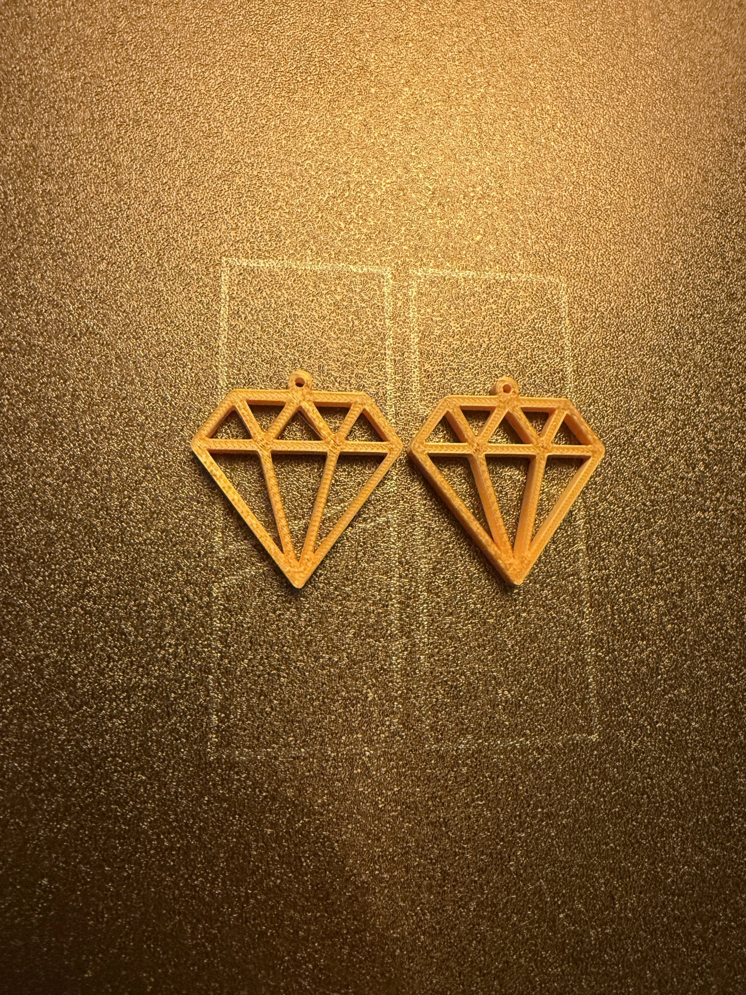 Two wooden diamond-shaped earrings with geometric cutouts on a glittery gold background.