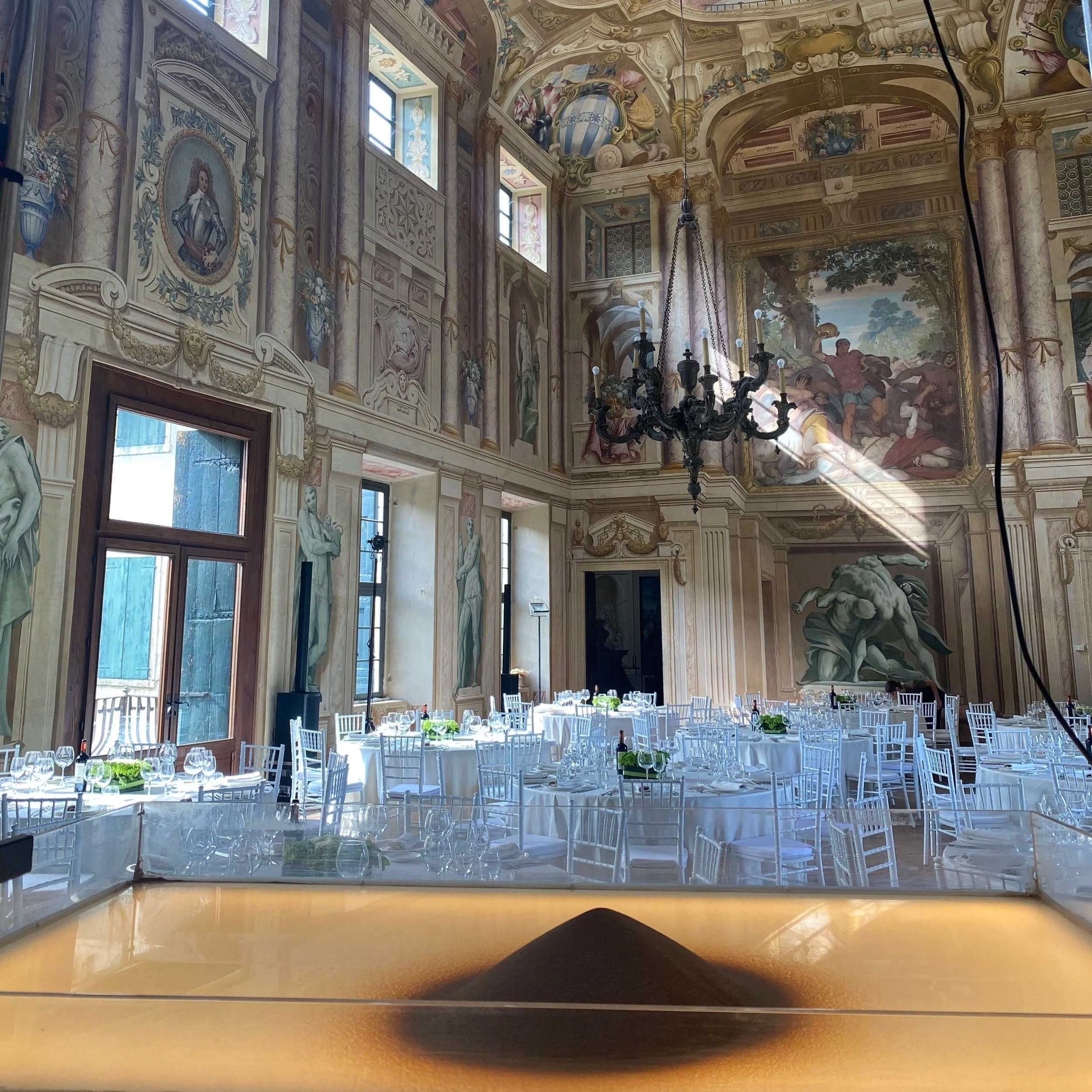 La sala affrescata di Villa Arvedi, Verona, allestita per una cena di gala, con il piano di lavoro e la sabbia di Nadia Pretto in primo piano prima dello spettacolo. Evento con Elisa Marai EM Event per Baywa-re sostenibilità