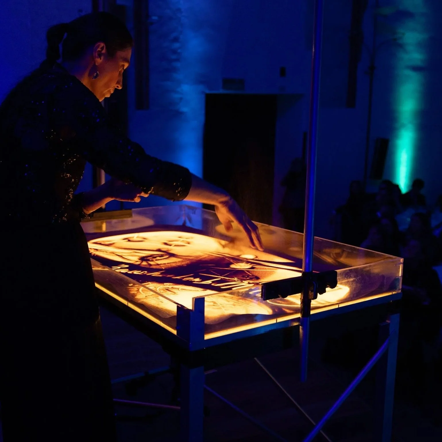 Nadia Pretto performance sand art, mentre disegna nella sabbia durante uno spettacolo, illuminata di blu nel buio della sala, corporate event