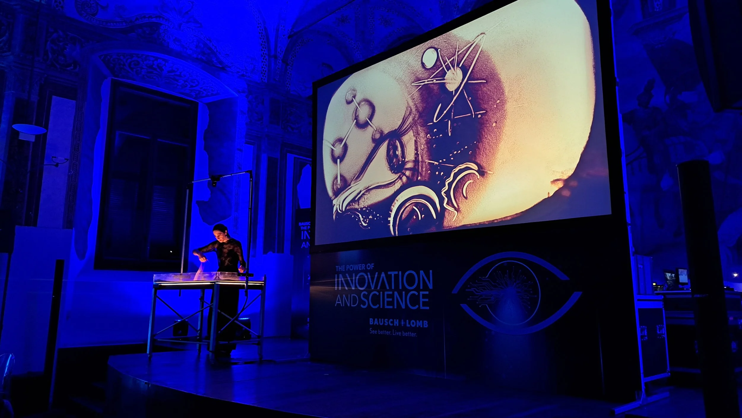 Spettacolo di sand art di Nadia Pretto evento corporate internazionale, chiostri di San Barnaba, Milano, con il disegno proiettato sul grande schermo