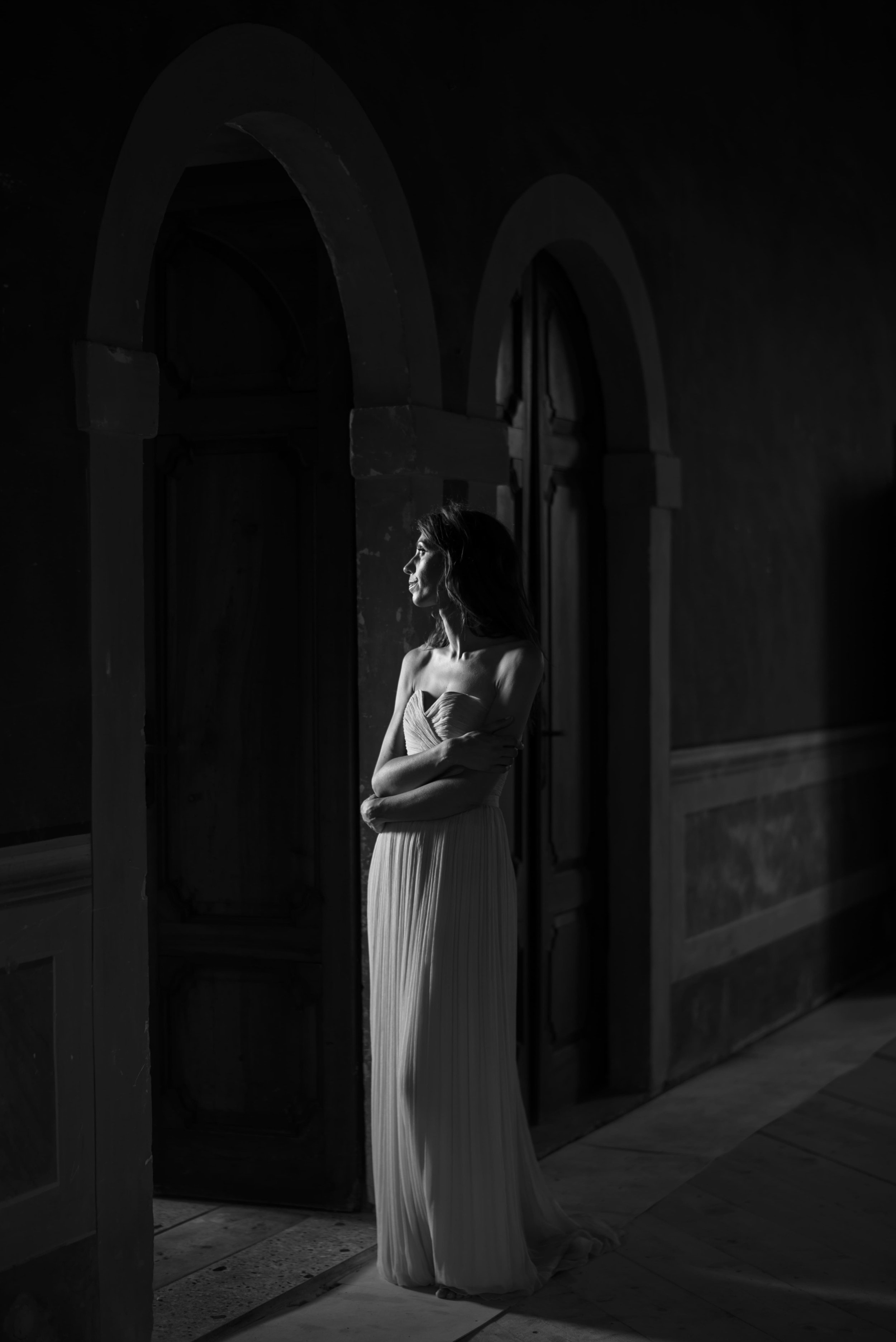 Nadia Pretto, artista, in bianco e nero sotto un arco, con un abito lungo chiaro