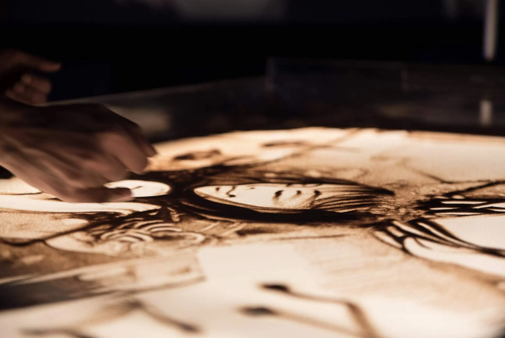Dettaglio di un disegno realizzato dal vivo nella sabbia, un volto, mano artista Nadia Pretto sand art