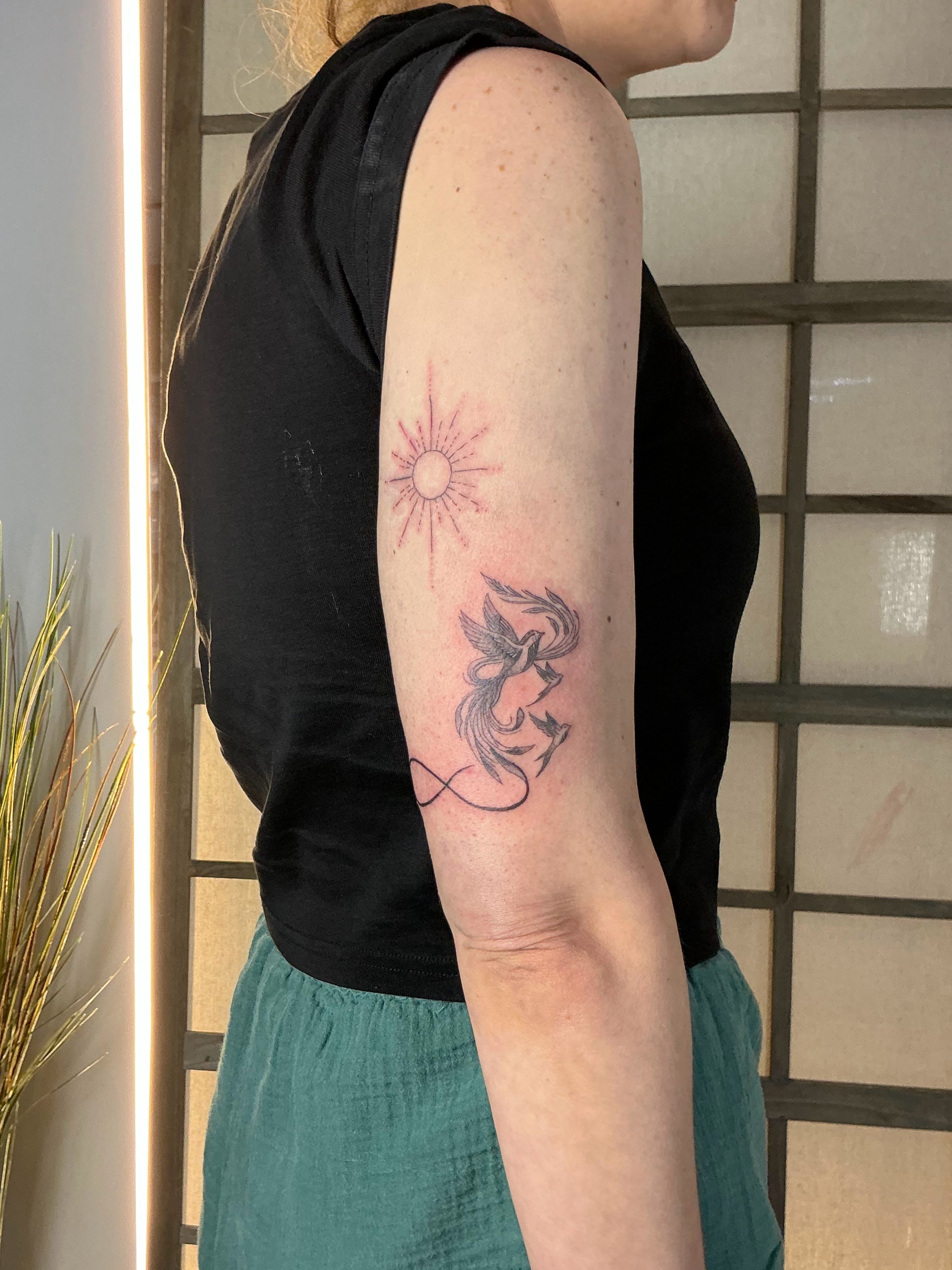 A tattoo of a sun, infinity, and birds on their upper arm.