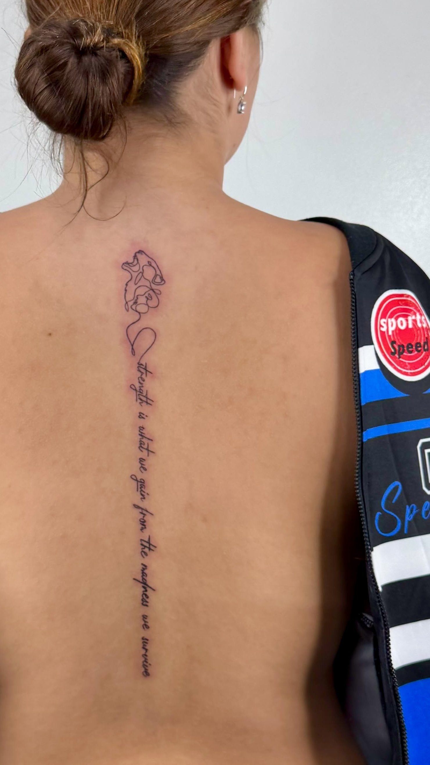 A tattoo along her back with handwritten cursive text and a line drawing of a woman's face.
