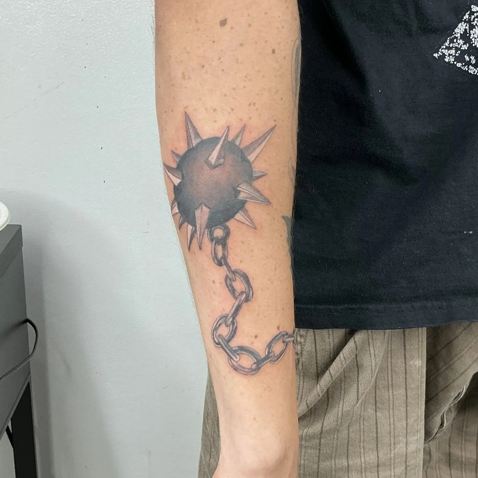 Tattoo of a spiked ball attached to a chain on person's forearm.