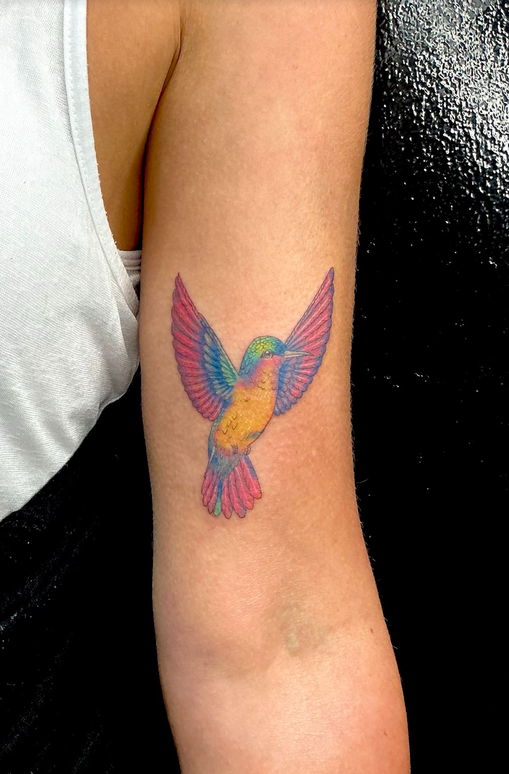 Colorful tattoo of a hummingbird on a person's upper arm.