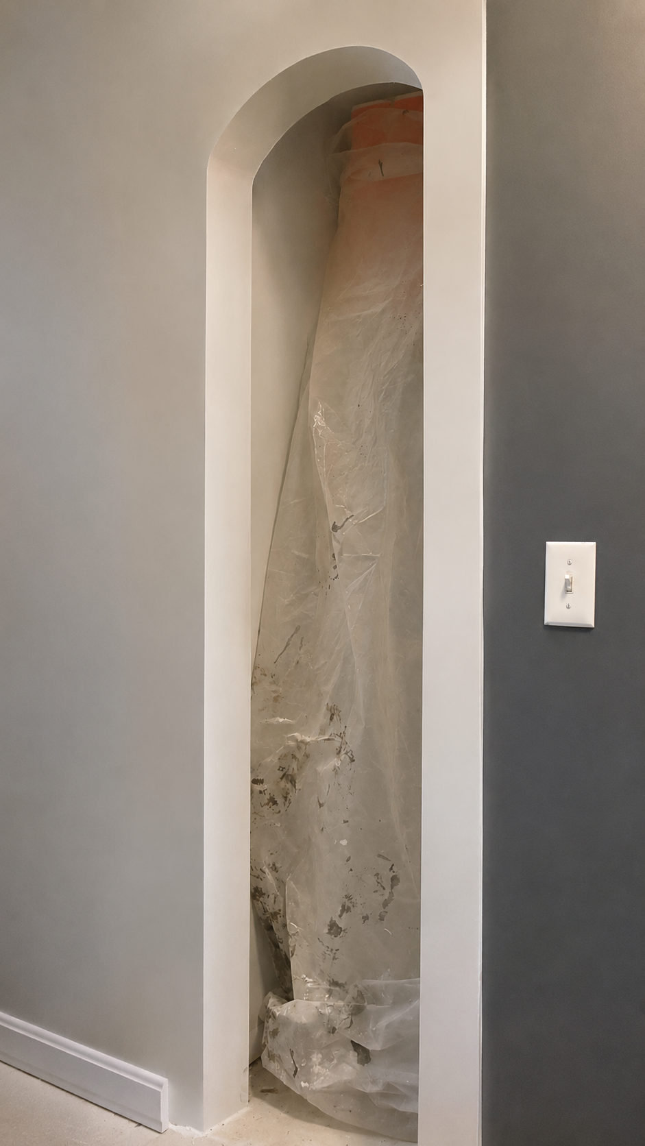 A tall, narrow, arched cutout in a wall revealing a wrapped marble sculpture inside a protective plastic covering.
