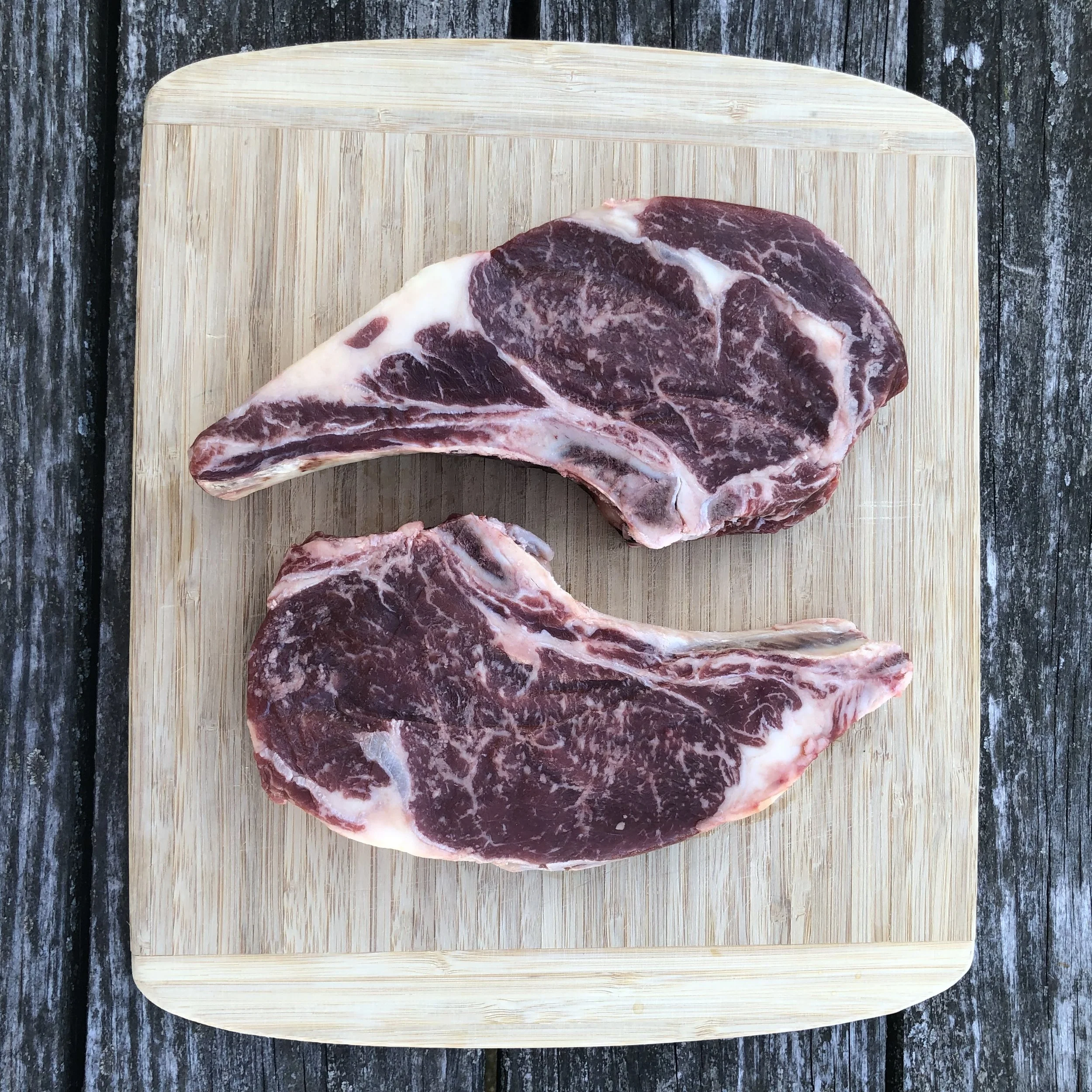 Raw beef steak on a wooden cutting board on a rustic outdoor wooden surface.