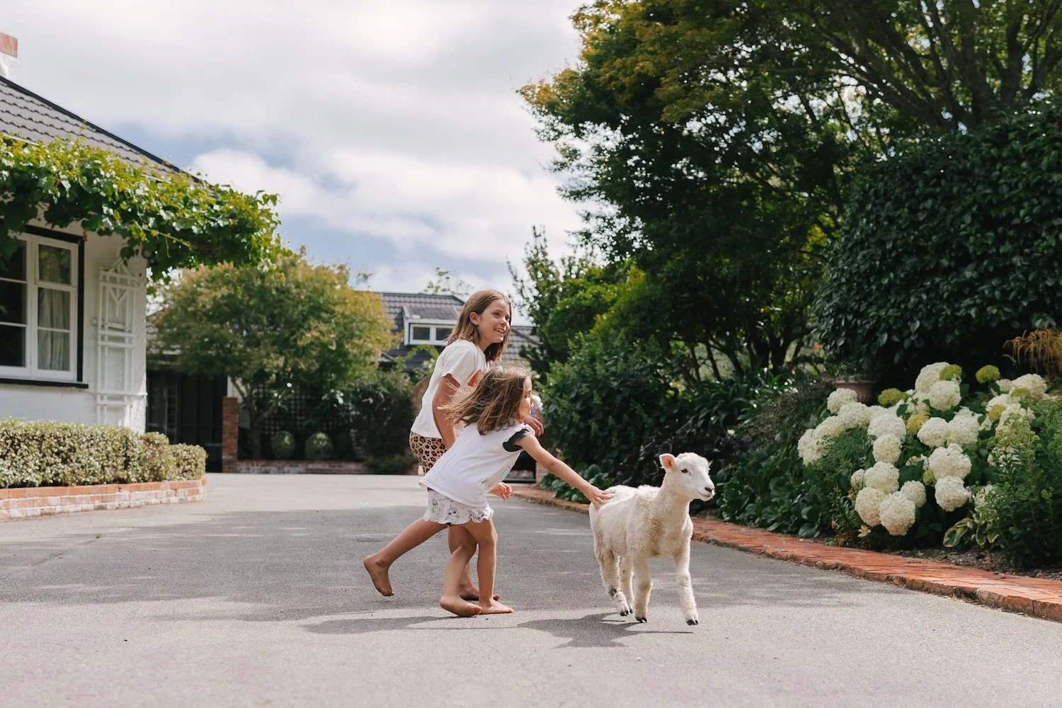Two young girls playing with a baby lamb on a at Rathmoy Estate with gardens and trees on a farm tour.