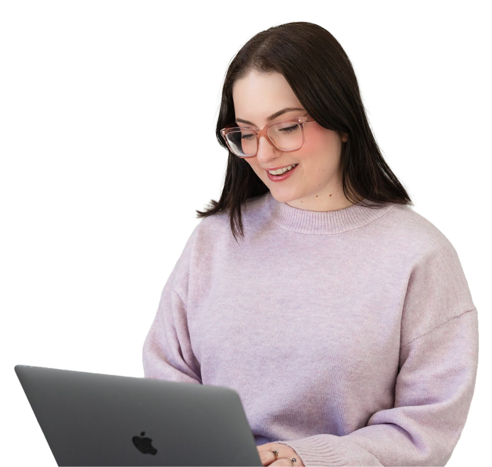 A young woman with brown hair and glasses smiling while looking at a silver MacBook laptop.