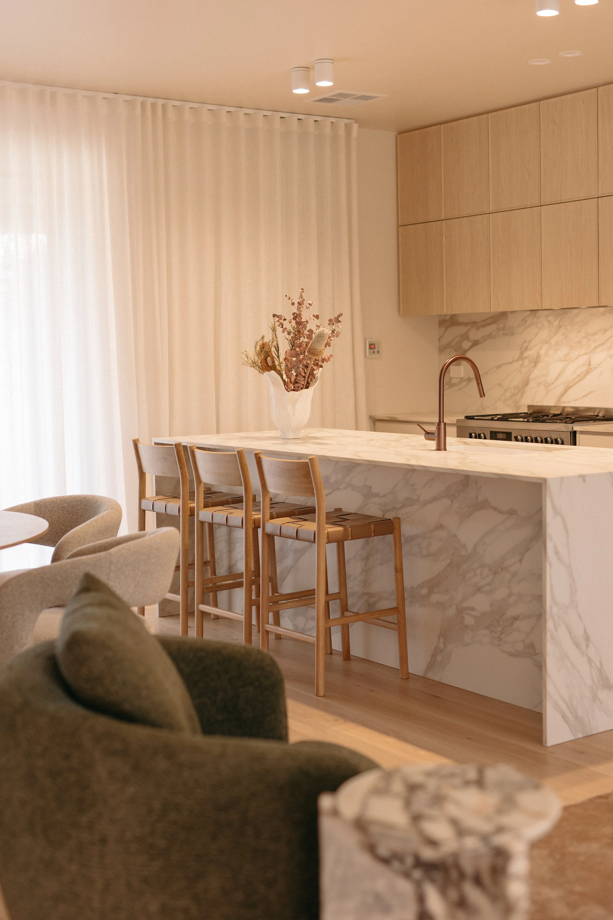 Modern kitchen with marble island, wooden cabinets, and dried flower centerpiece, illuminated by ceiling lights.