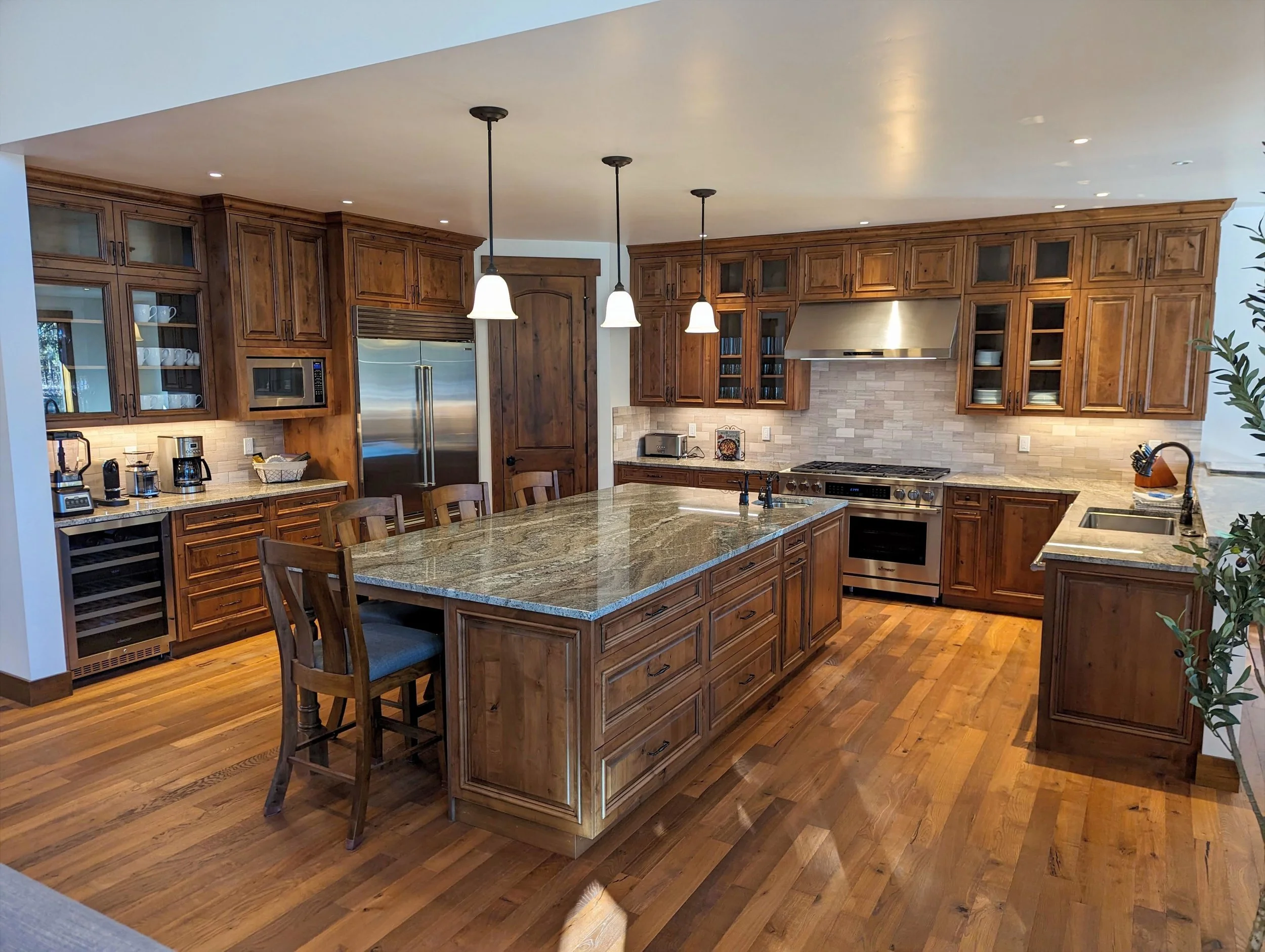 A spacious kitchen with wooden cabinets, a large island with a granite countertop, stainless steel appliances, and hanging pendant lights.