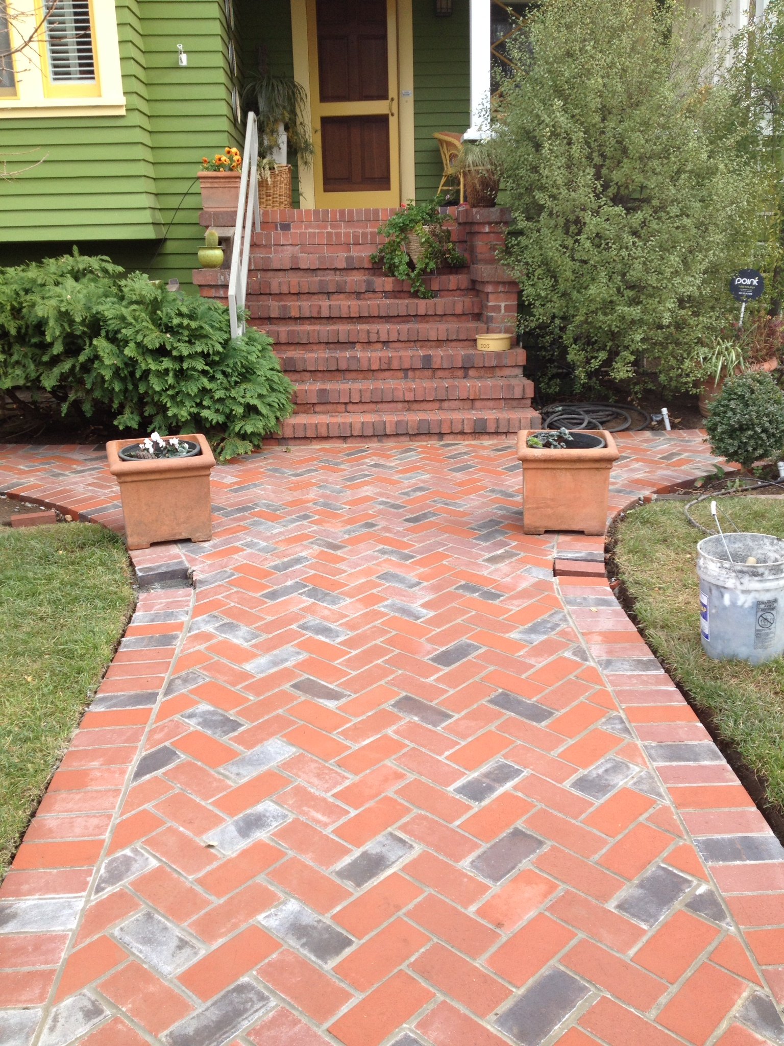 Brick entry steps with potted plants, green house siding, and a front door.