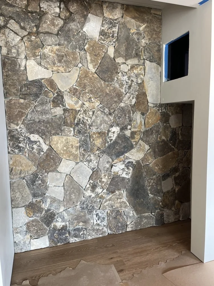 Interior wall with irregularly shaped stone tiles, partially framed by architectural corner, with wooden flooring.