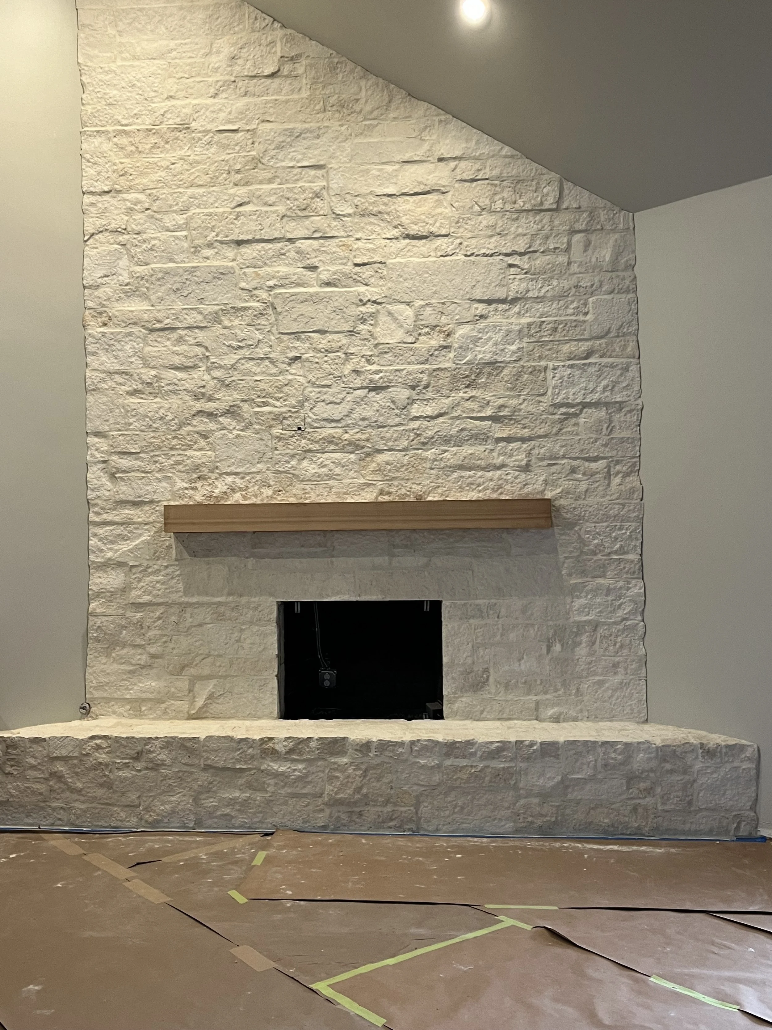 Under construction interior with a white brick fireplace, a wooden mantel, and taped-off floor space.