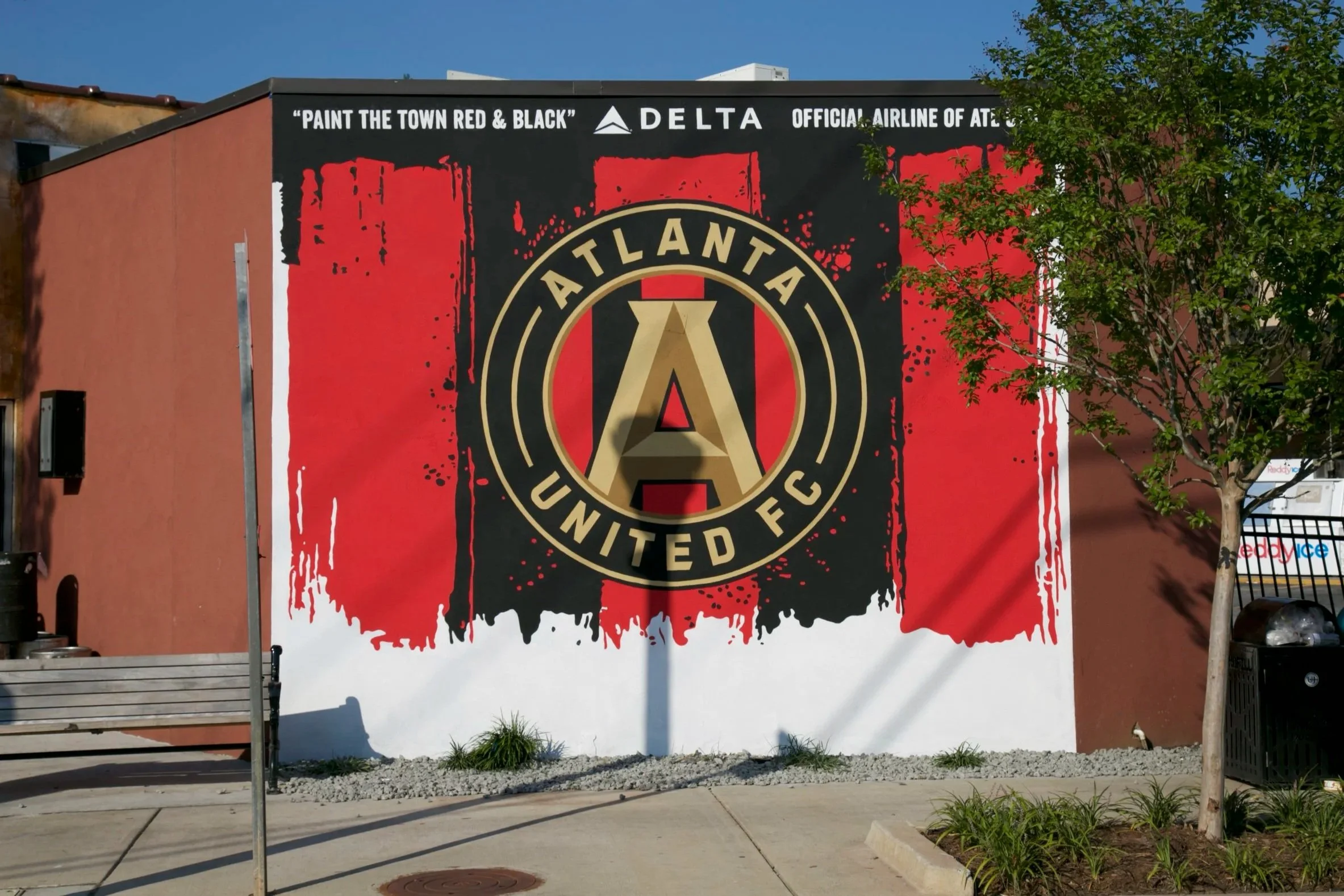 Large mural on a building featuring the Atlanta United FC logo with red, black, and gold design elements. The mural includes the phrase 'Paint the Town Red & Black' and branding for Delta Airlines.
