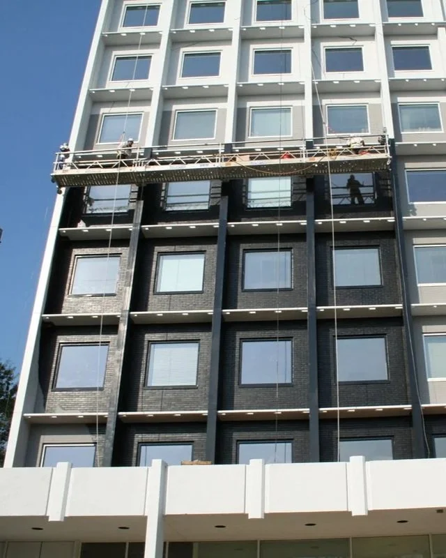Construction workers on a suspended scaffold working on a modern multi-story building with a white and black facade.