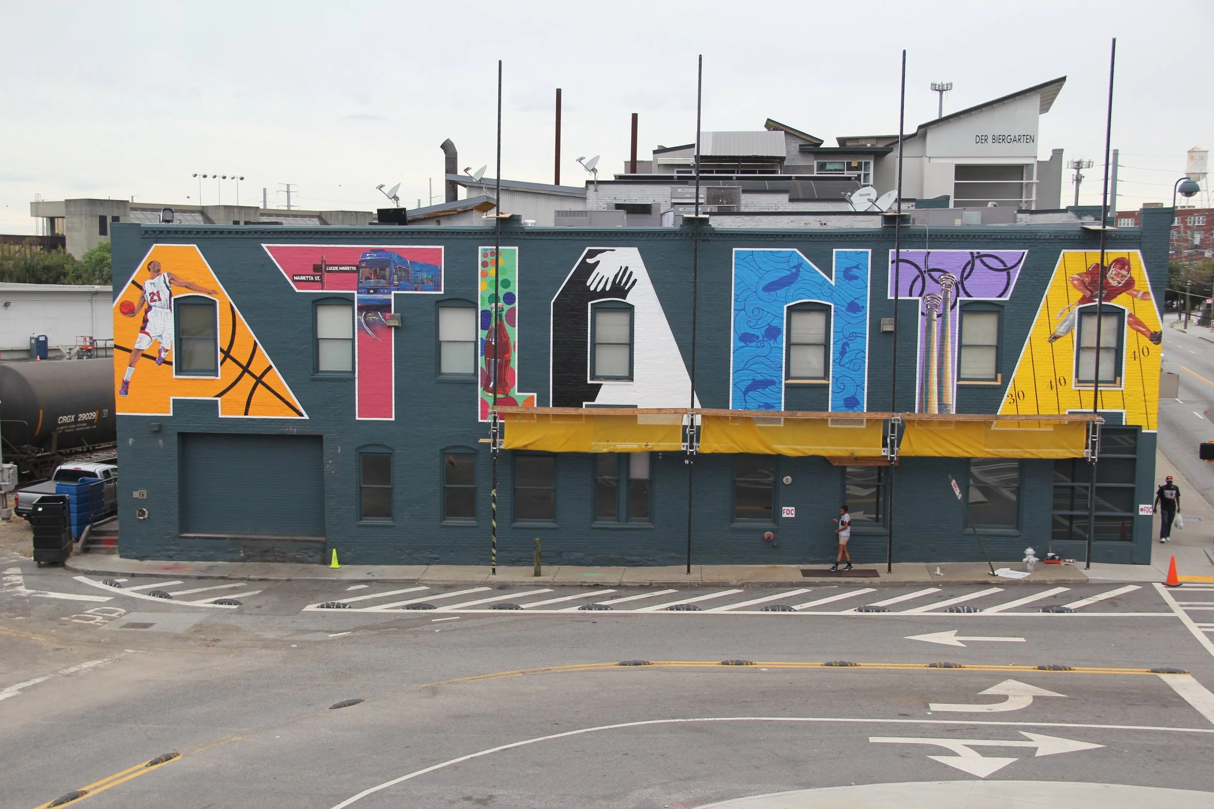 Colorful mural on a building wall featuring a basketball player, cityscape, hand, fish, and sports equipment.