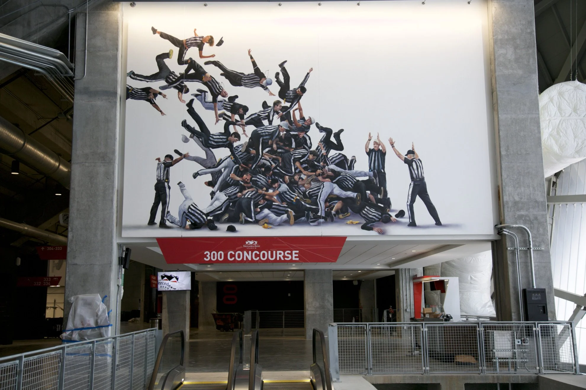 Large poster of multiple people dressed as referees in black and white striped shirts, piled on top of each other, at the Mercedes-Benz stadium. The poster displays the text '300 CONCOURSE' below it.