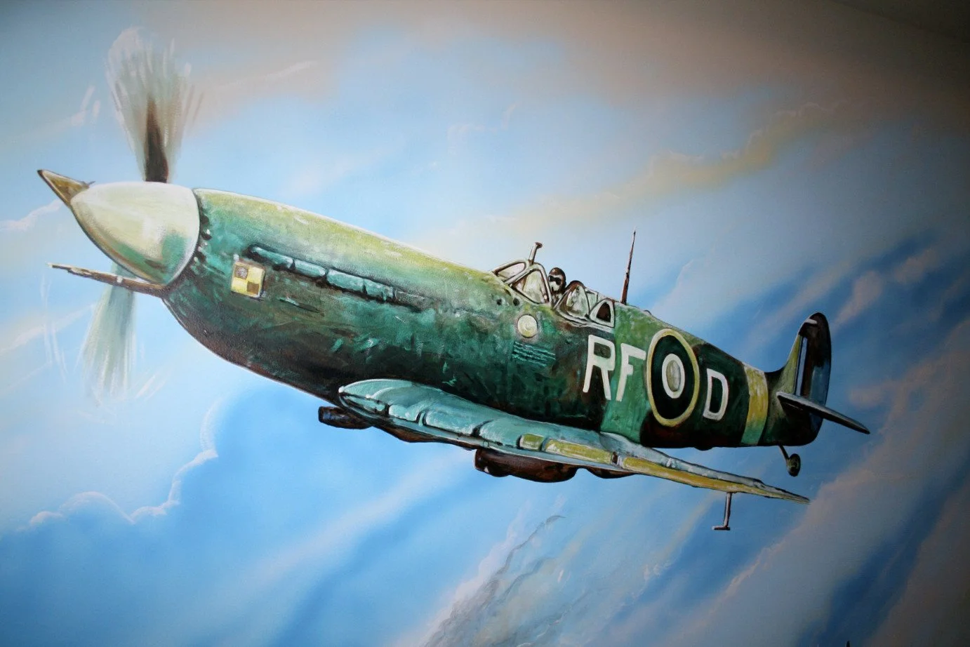 A mural of a World War II fighter plane flying through the sky, painted in shades of green with the markings 'RF D' on the side.