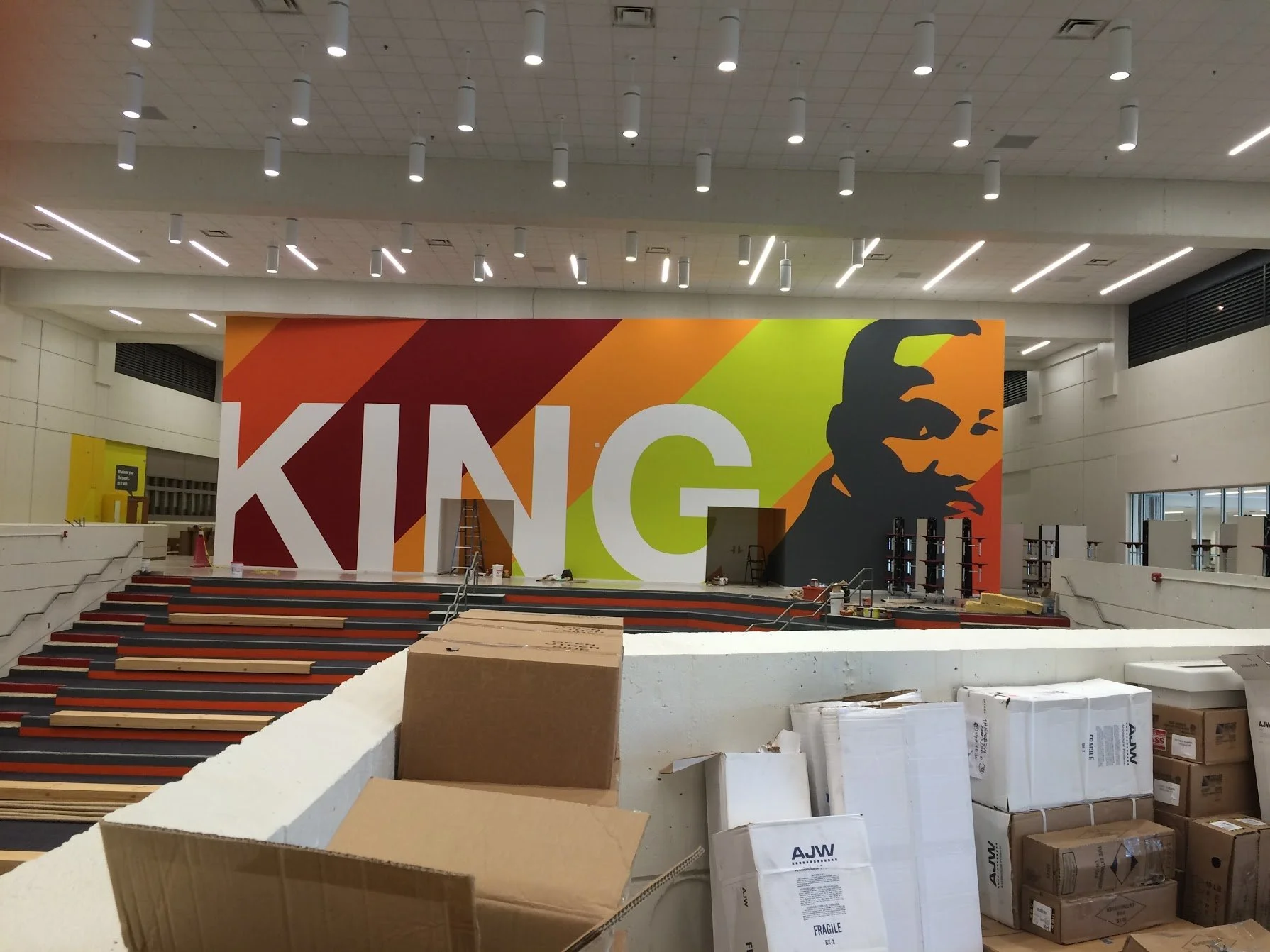 Interior of a large retail store under construction, with a prominent colorful mural of Martin Luther King Jr. and the word 'KING' on the wall. Construction materials and equipment are scattered around.