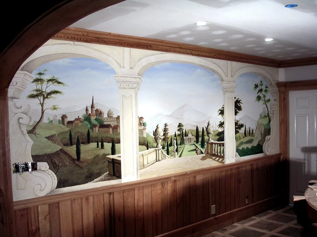 Wall mural depicting a scenic landscape with rolling hills, a castle, cypress trees, and mountains in the background, framed by classical architectural elements.