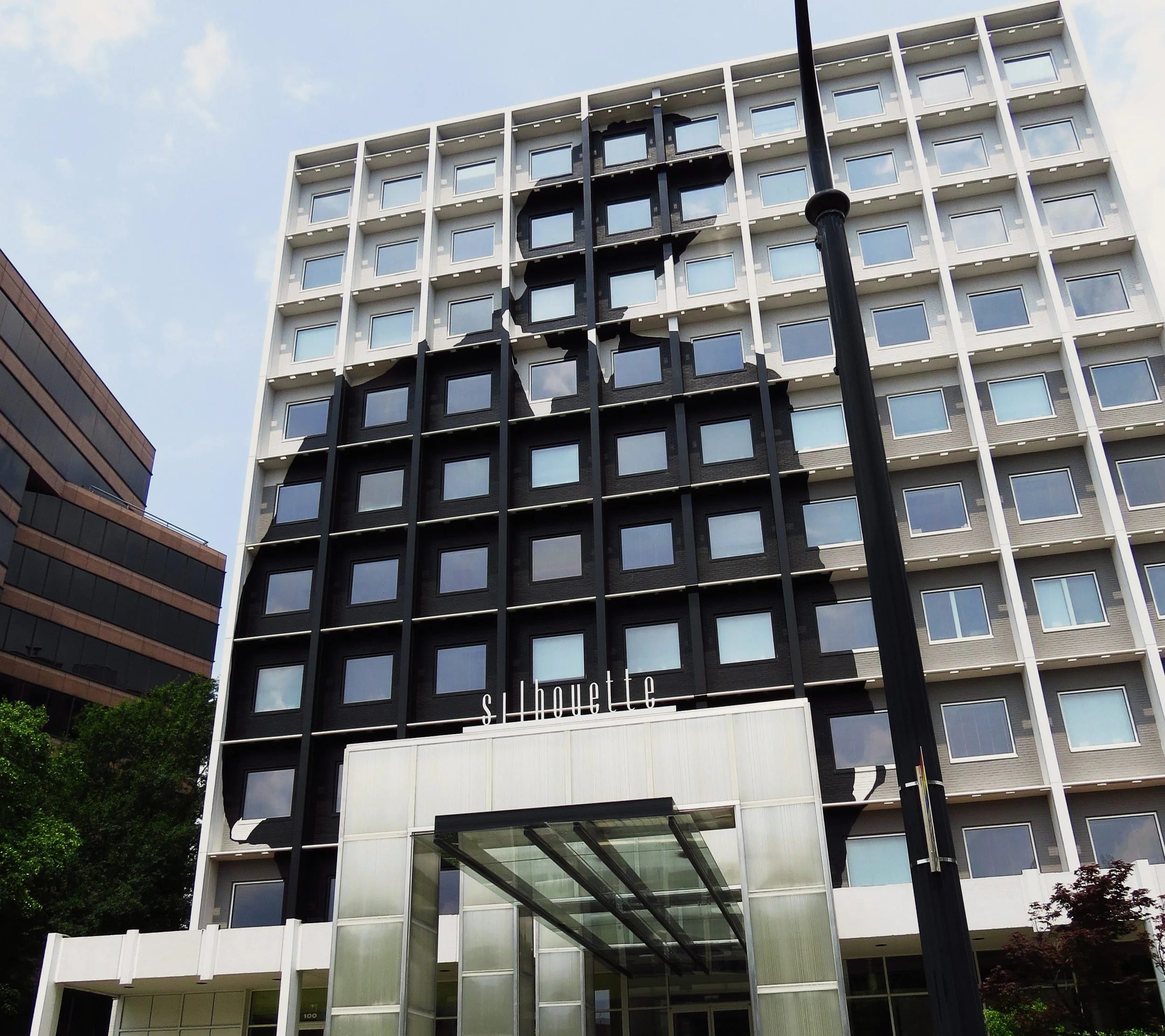 Modern multi-story building with large glass windows and white framing, with a black section running vertically, and a sign that reads 'the house' on the lower part of the building.