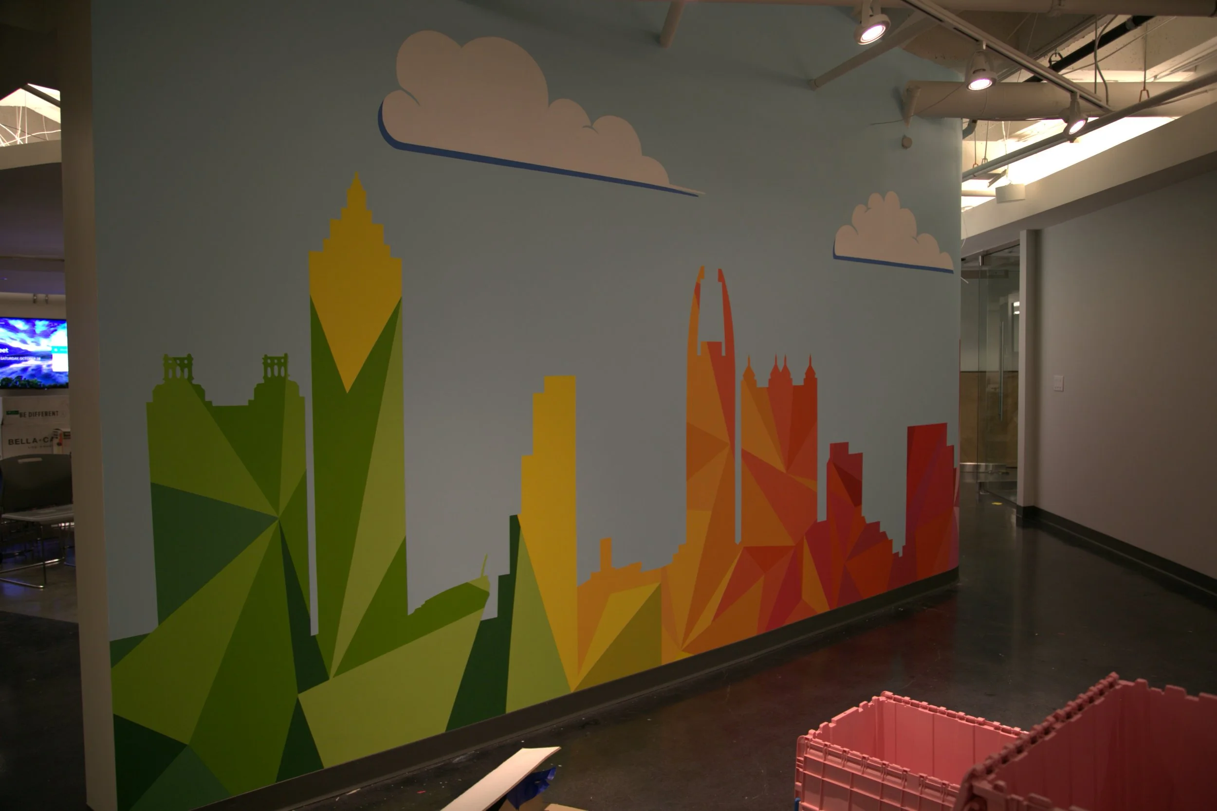 Colorful wall mural depicting stylized skyline and cloud shapes in blue, green, yellow, orange, and red sections inside a modern building.