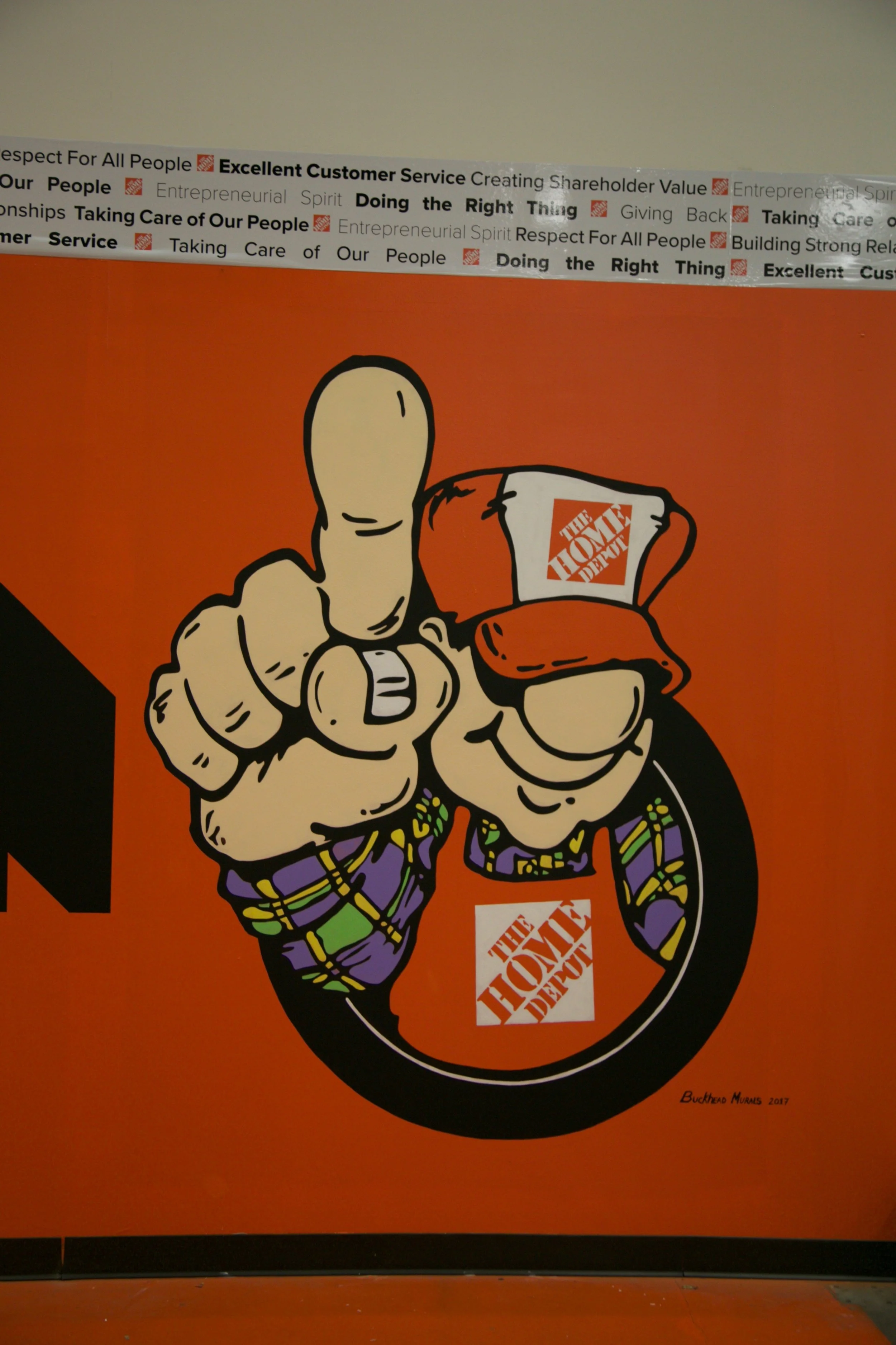 Mural with cartoon hand pointing towards the viewer holding a mug with 'The Home Depot' logo, with text at the top about excellent customer service and taking care of people.
